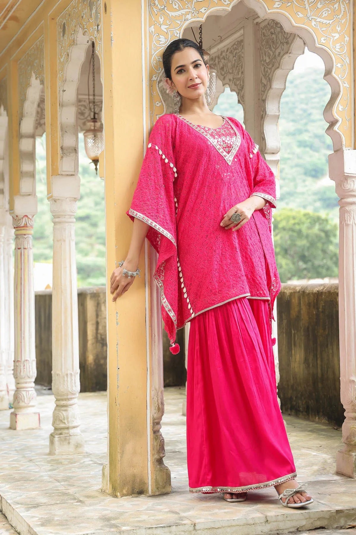 Woman in a pink traditional outfit standing in an ornate architectural setting.