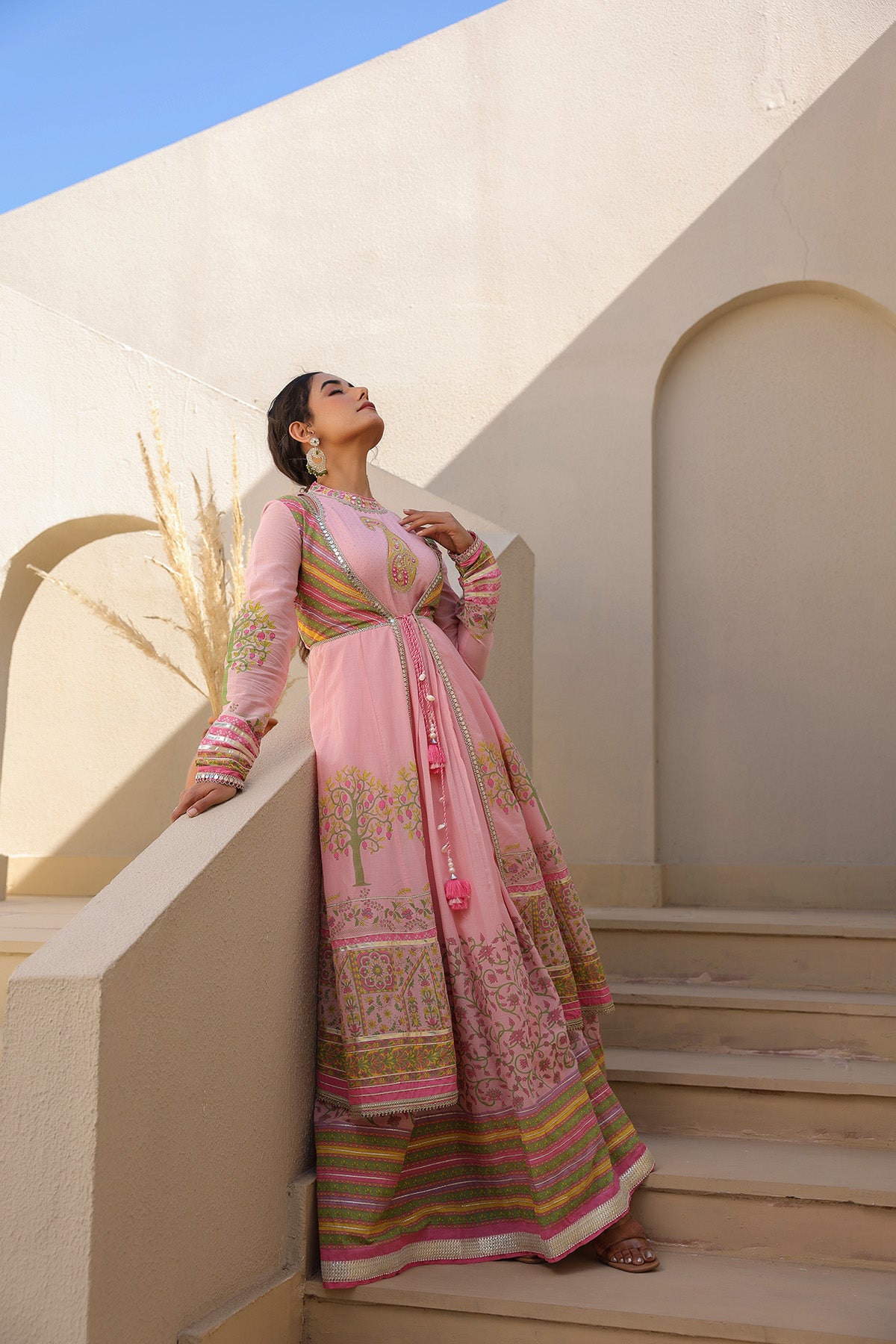 Woman in a traditional pink and gold dress standing on steps with a neutral background