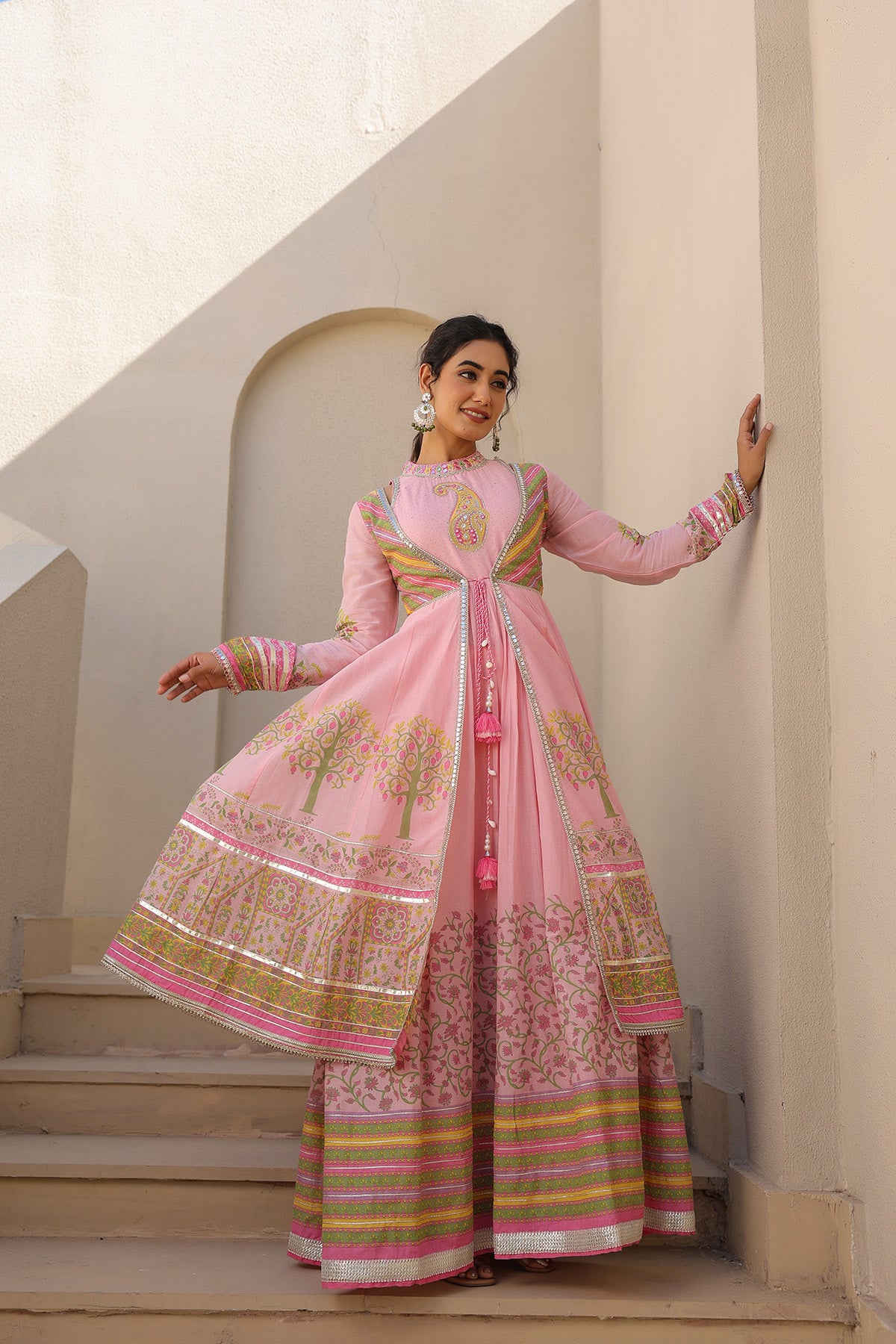 Woman in a traditional pink and gold outfit standing on steps with a neutral background