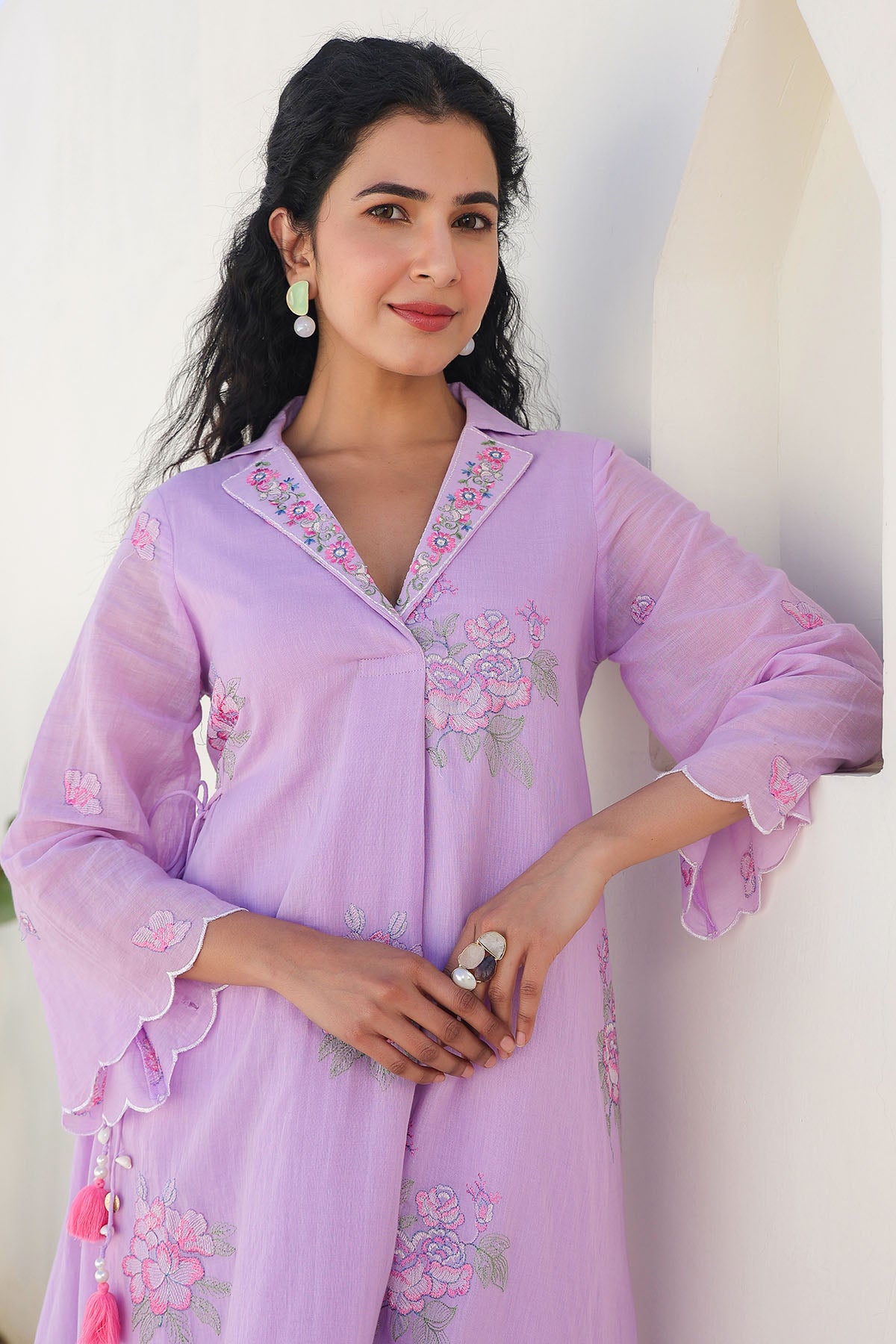 Woman wearing a light purple embroidered outfit against a white background