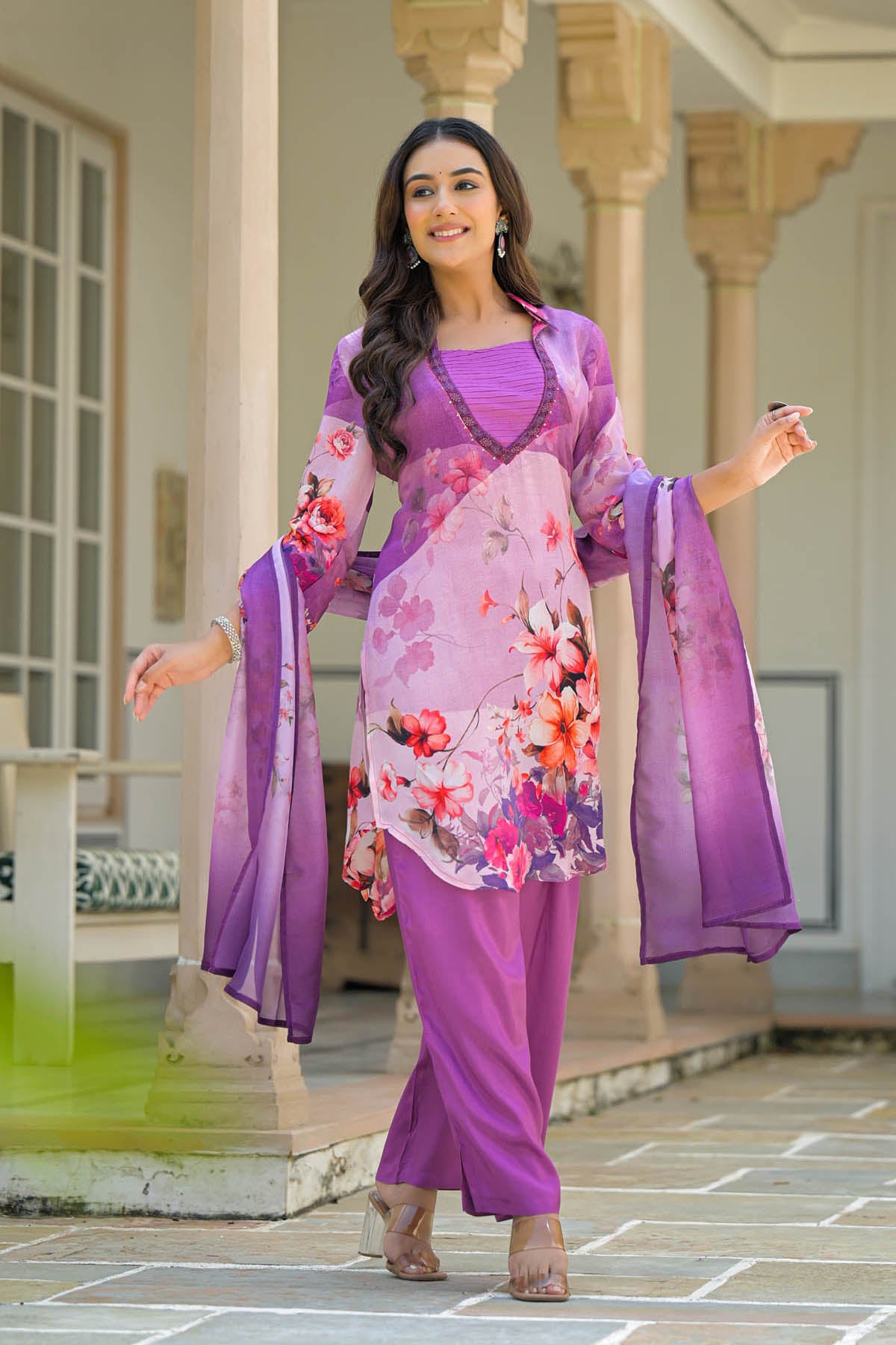 Woman in a traditional outfit with floral patterns standing in front of a building.