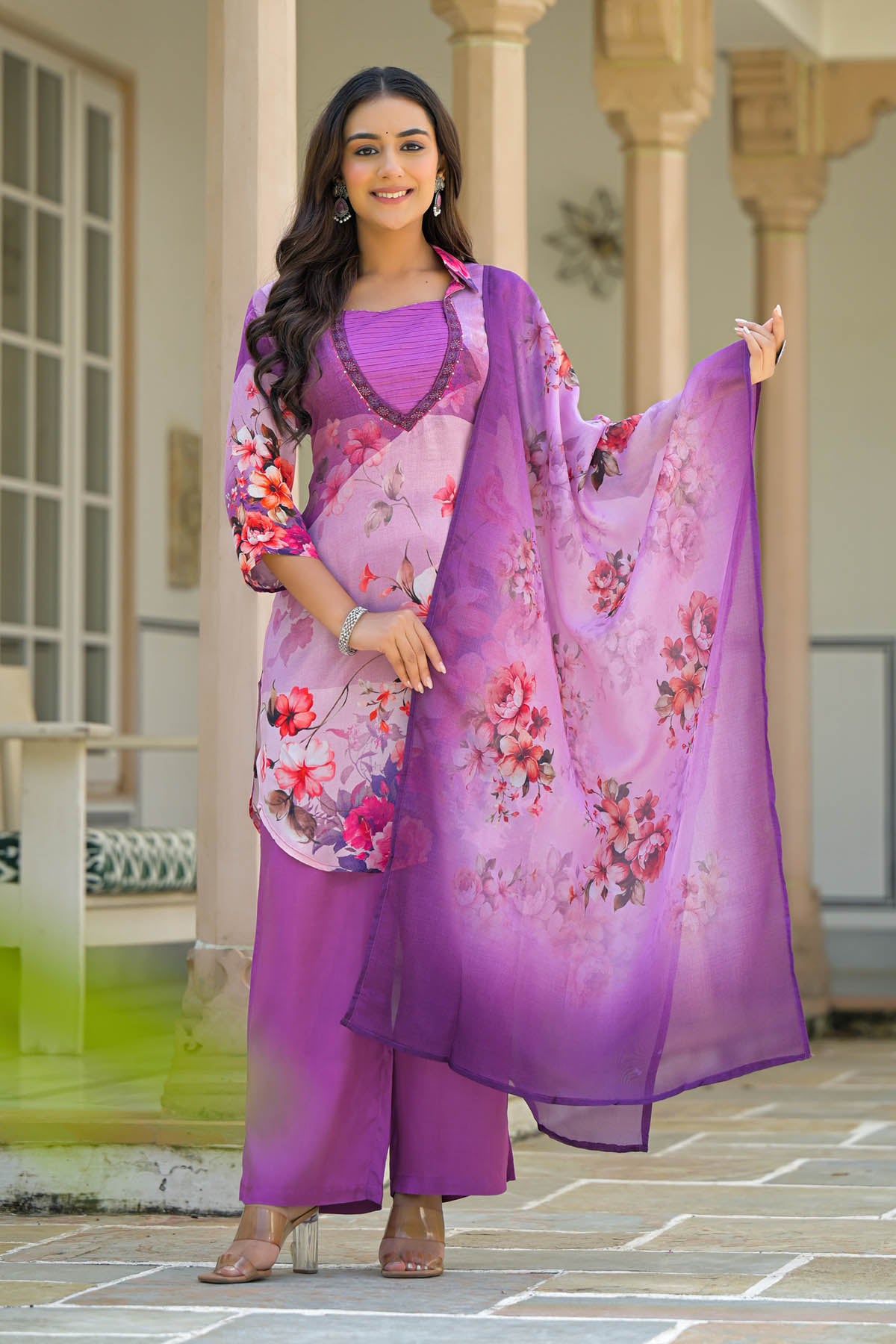 Woman wearing a purple floral outfit standing in front of a building with columns.