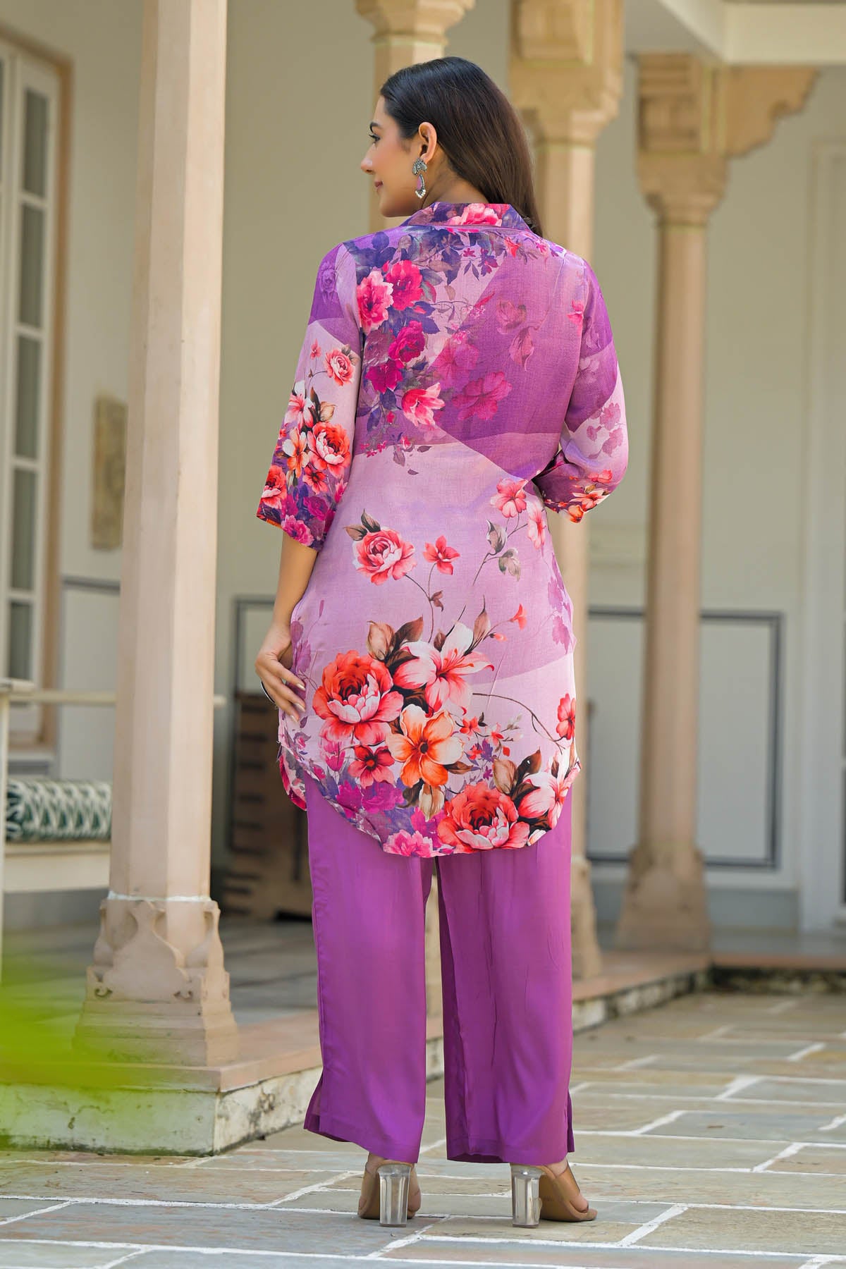 Woman wearing a vibrant floral outfit in an outdoor setting with columns.