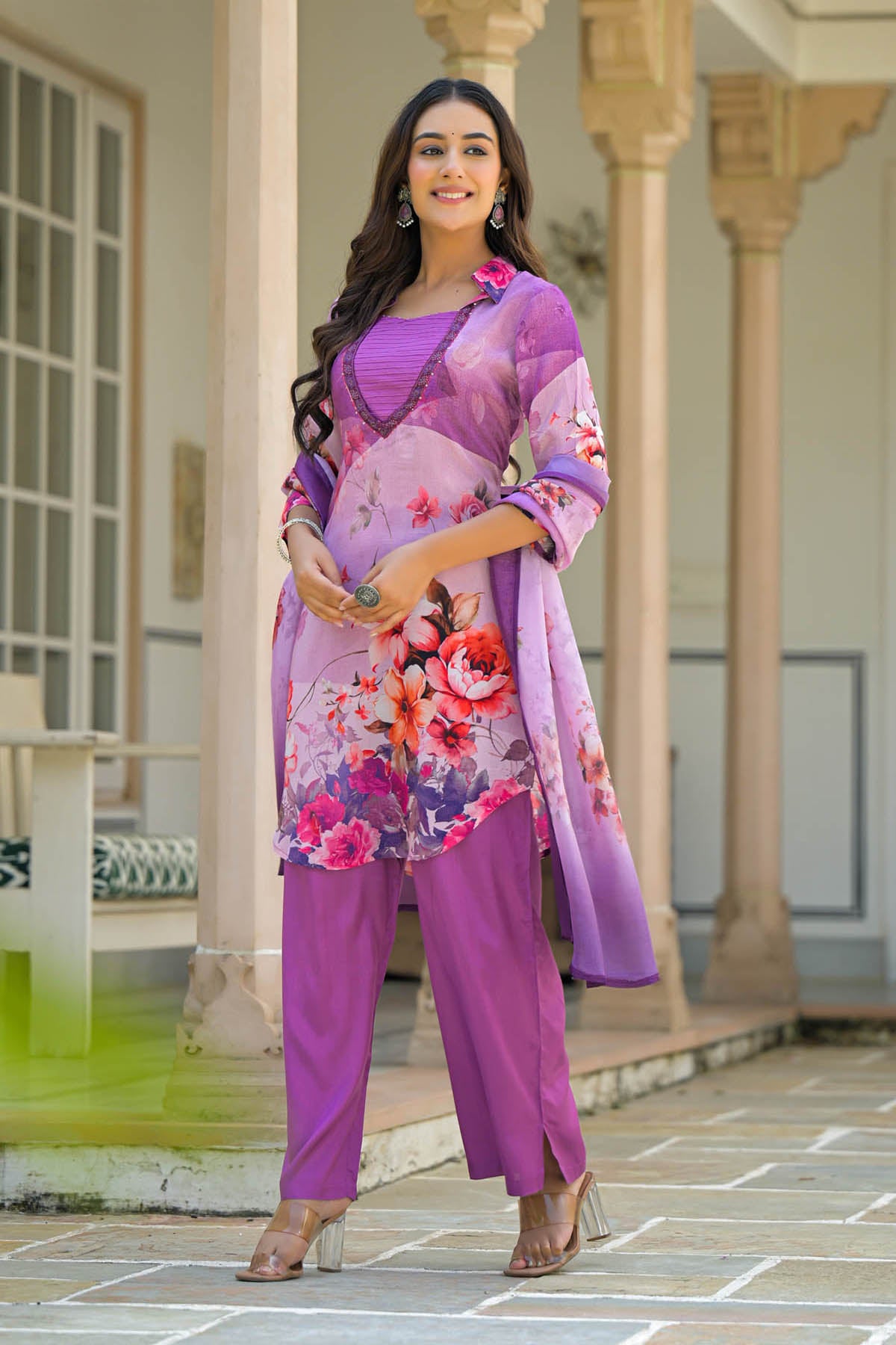 Woman in a floral purple outfit standing in front of architectural columns.