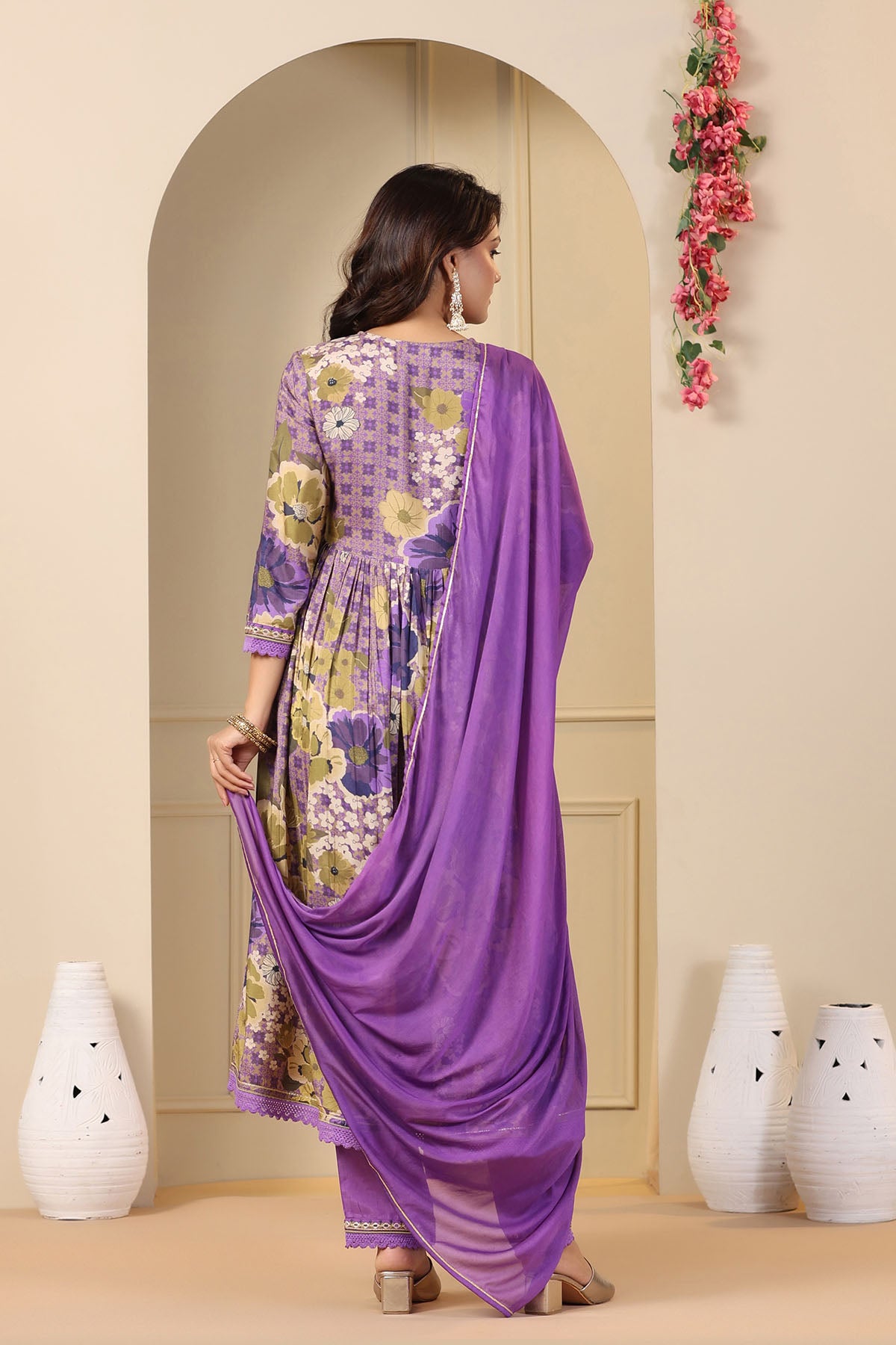 Woman wearing a purple floral dress with a matching dupatta in a decorated room.