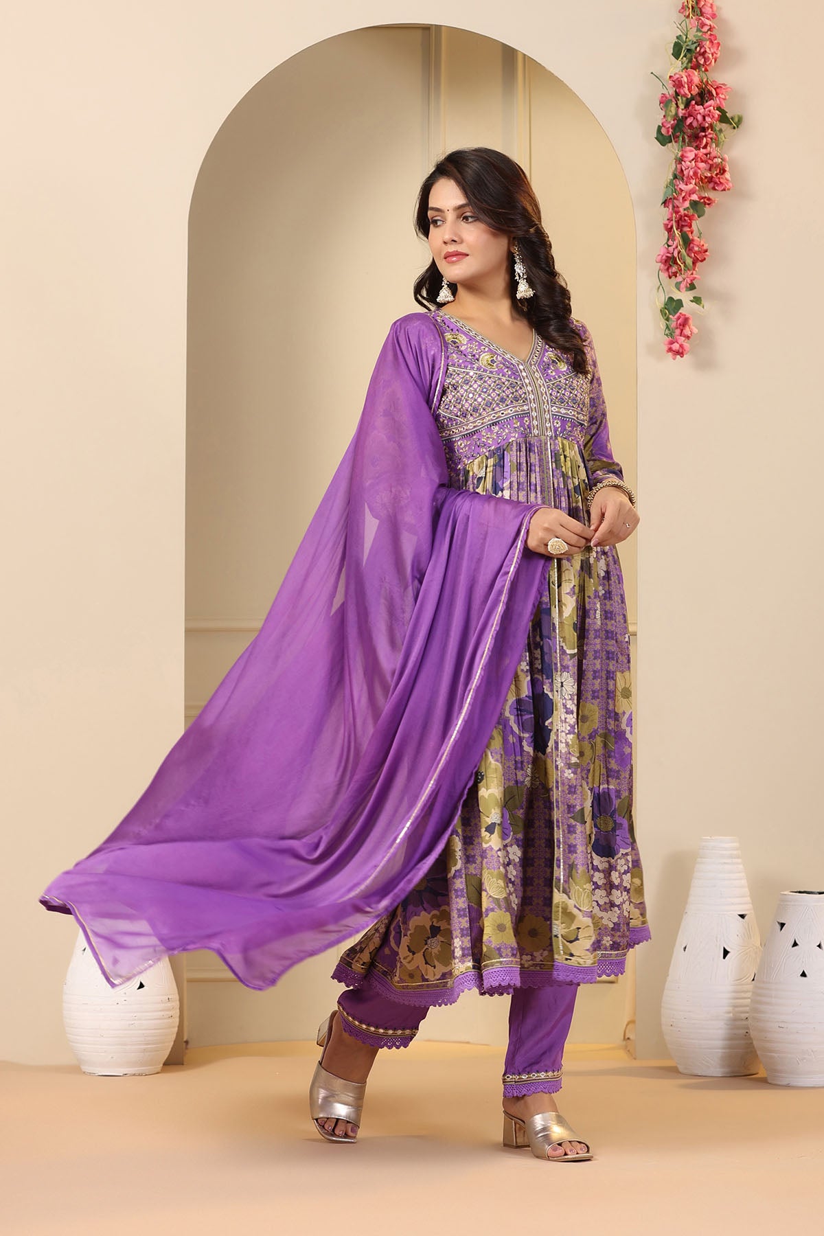 Woman wearing a purple traditional outfit with floral patterns in a decorated room.