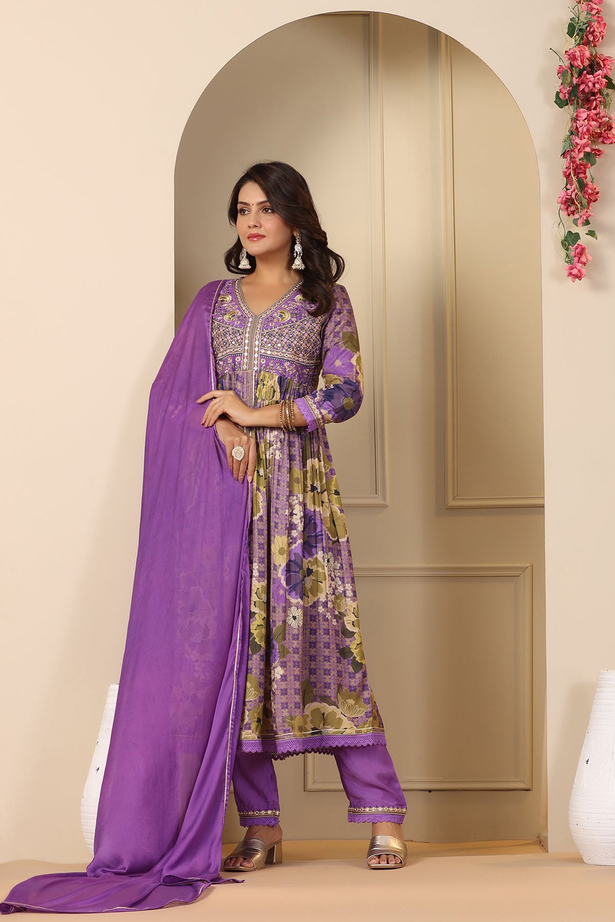 Woman wearing a purple traditional outfit with floral patterns in a decorated room.