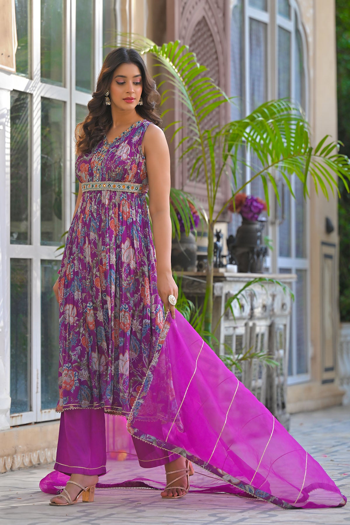 Woman in a colorful dress with a pink dupatta standing in front of a glass door.