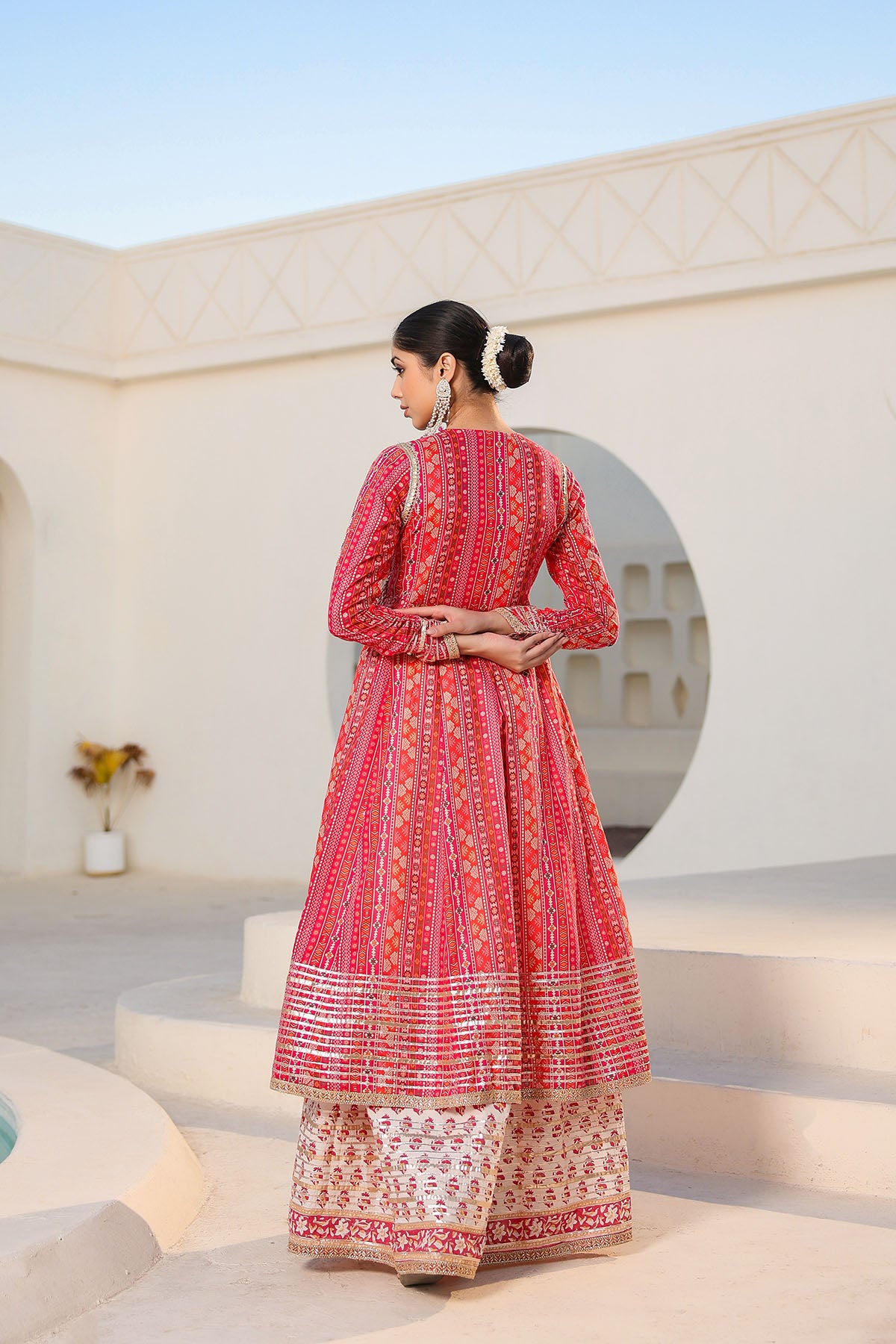 Woman in a red and white traditional outfit standing in a sunlit architectural setting.