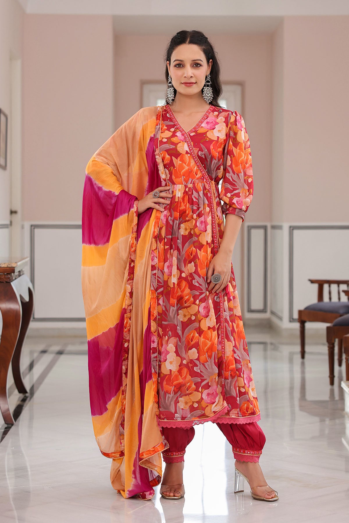 Woman in a colorful traditional outfit with a pink and orange dupatta in a well-lit room.