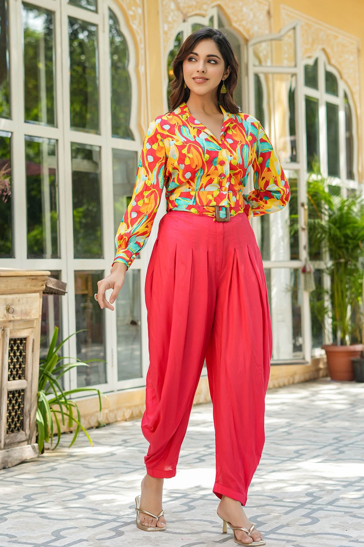 Woman wearing a colorful blouse and red pants standing outdoors.