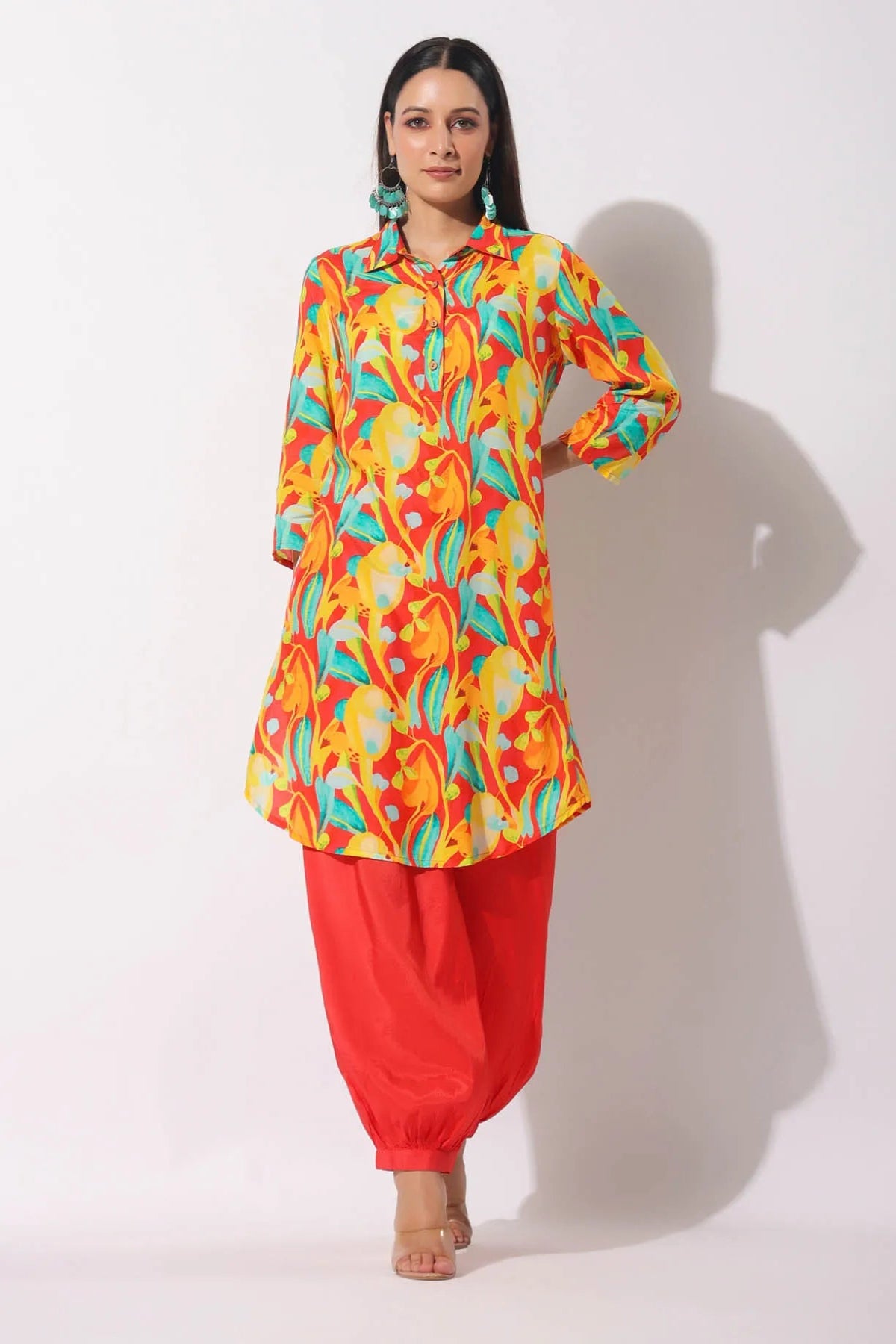 Woman wearing a colorful patterned top and red pants on a white background
