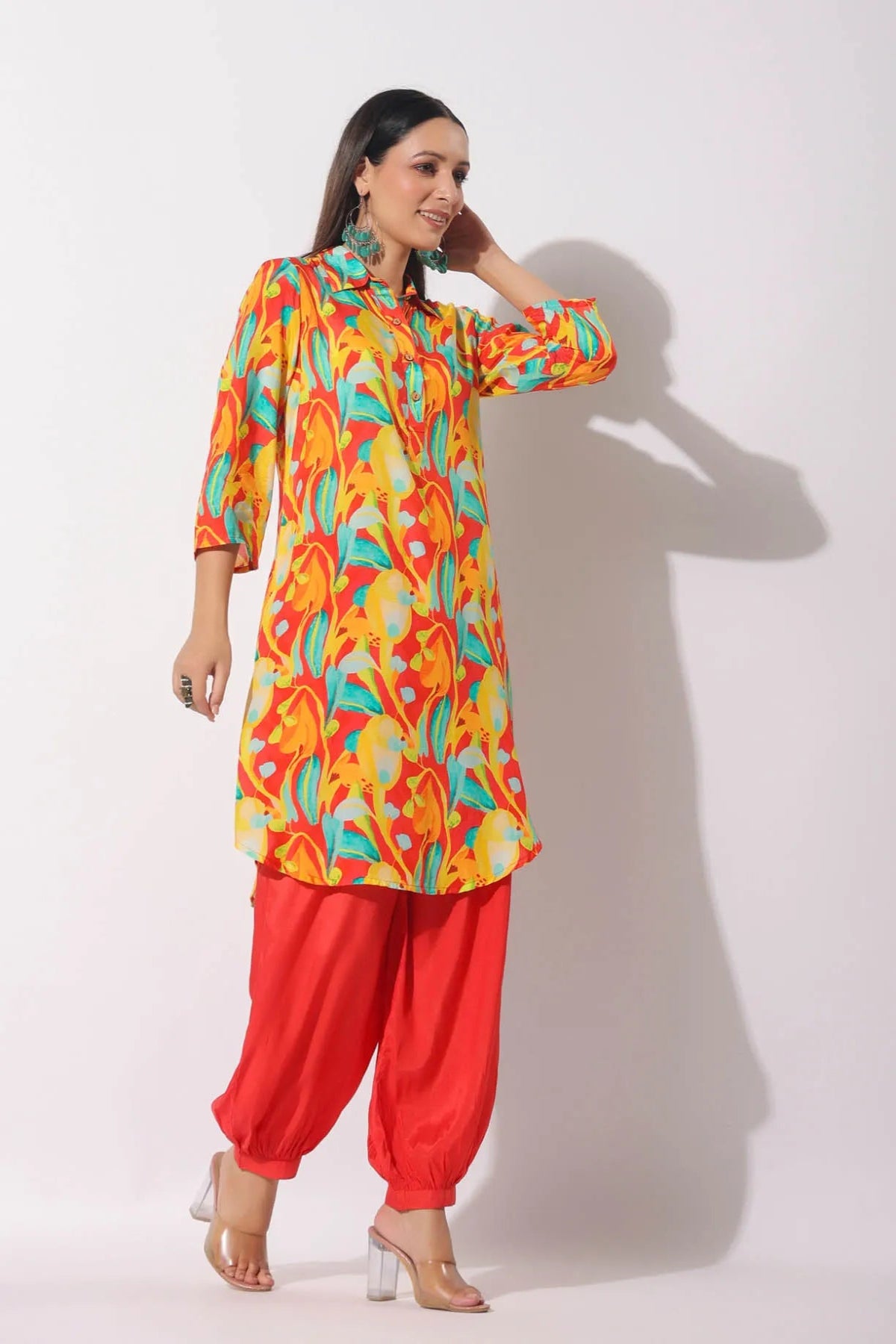 Woman wearing a colorful top and red pants against a white background