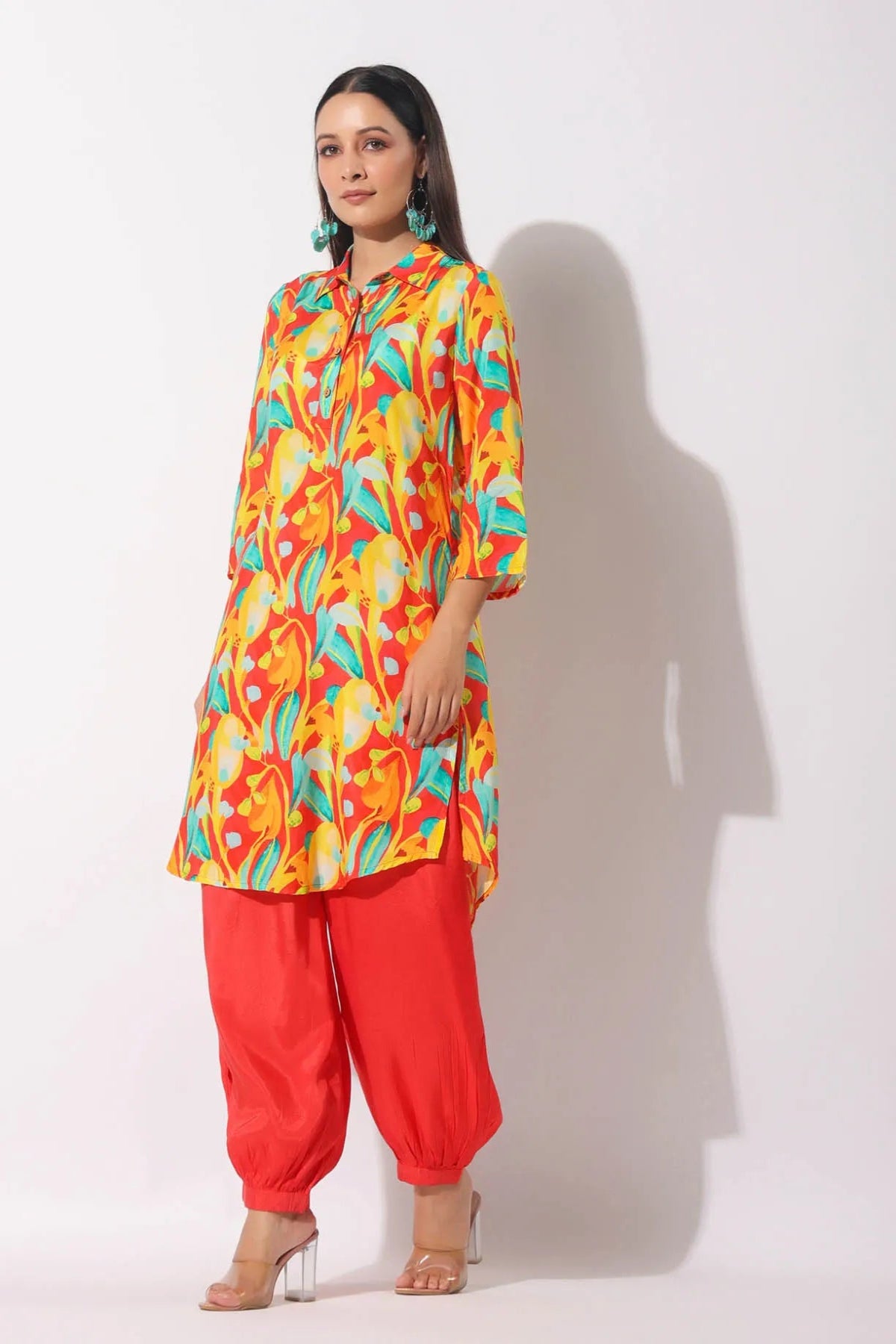Woman wearing a colorful patterned kurta with red pants on a white background