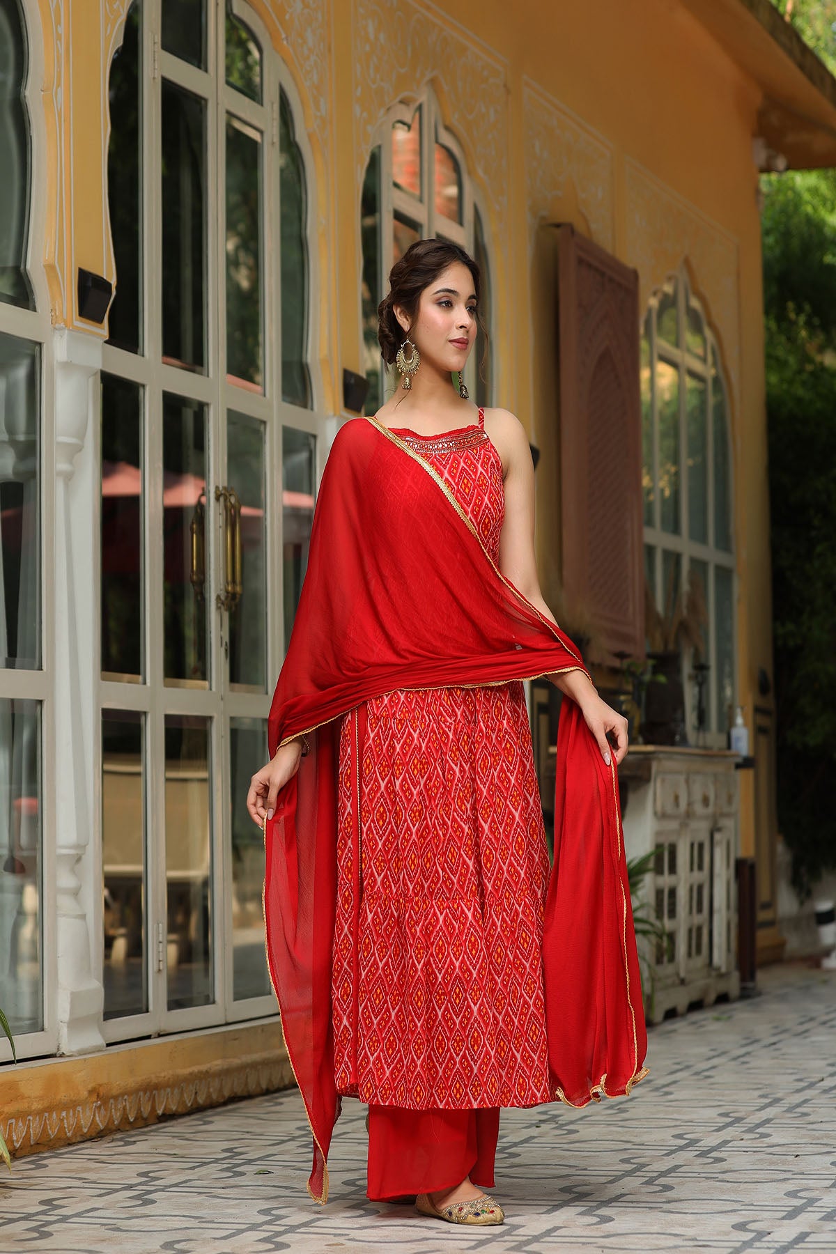 Woman in a red traditional outfit standing in front of a decorative building entrance.
