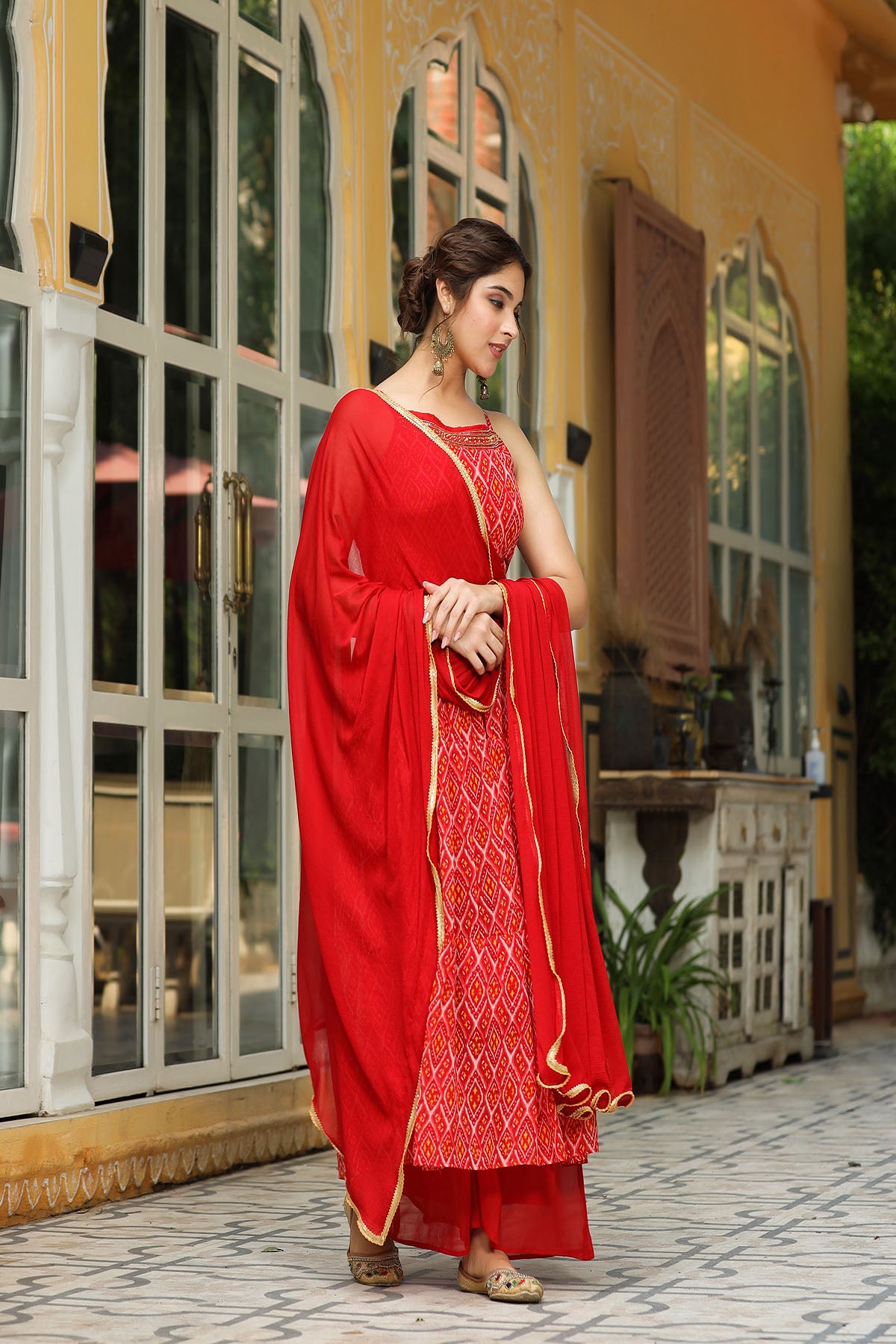 Woman in a red traditional outfit standing in front of a decorative building entrance.