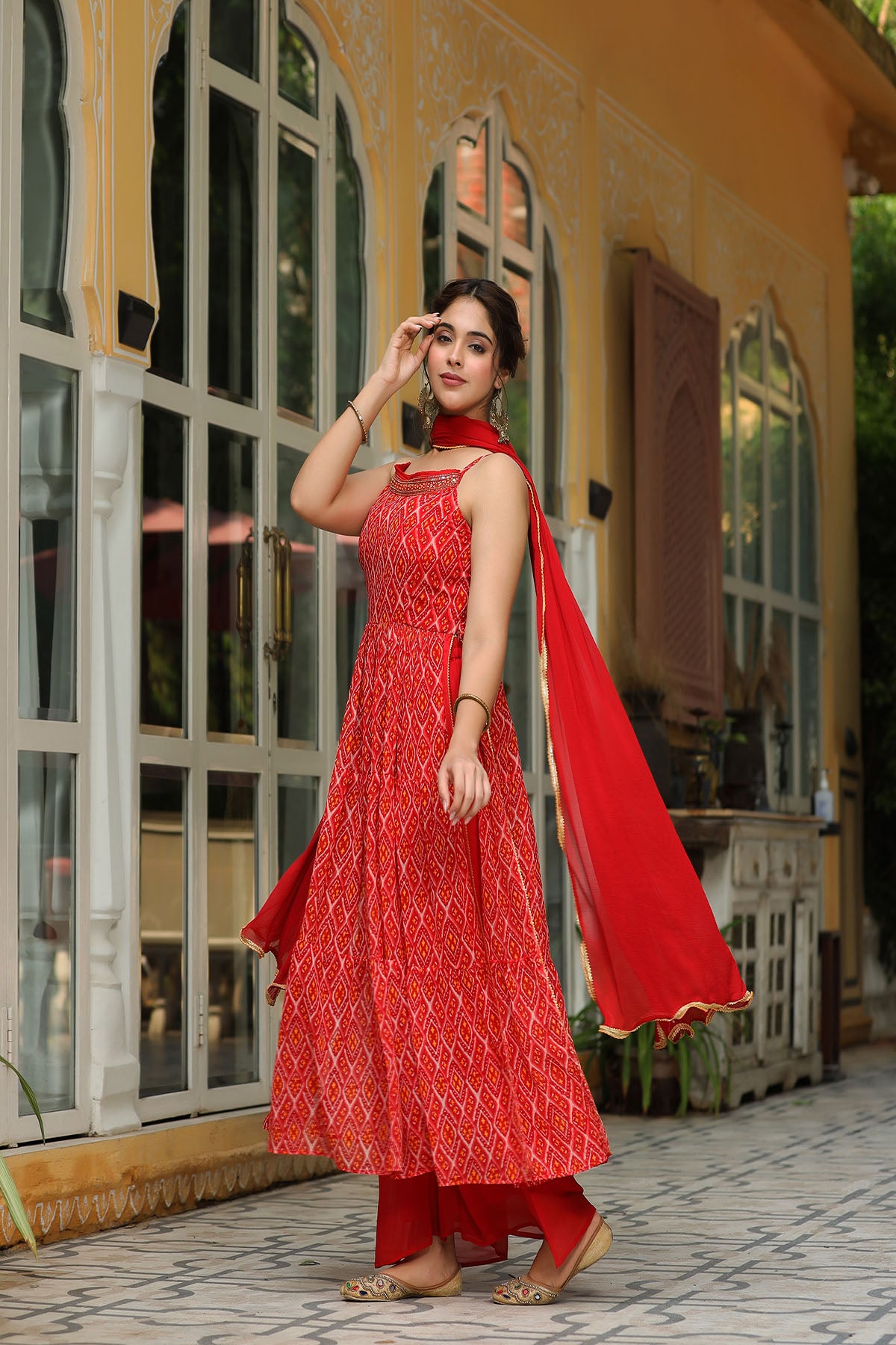 Woman in a red traditional outfit standing in front of a building with large windows.