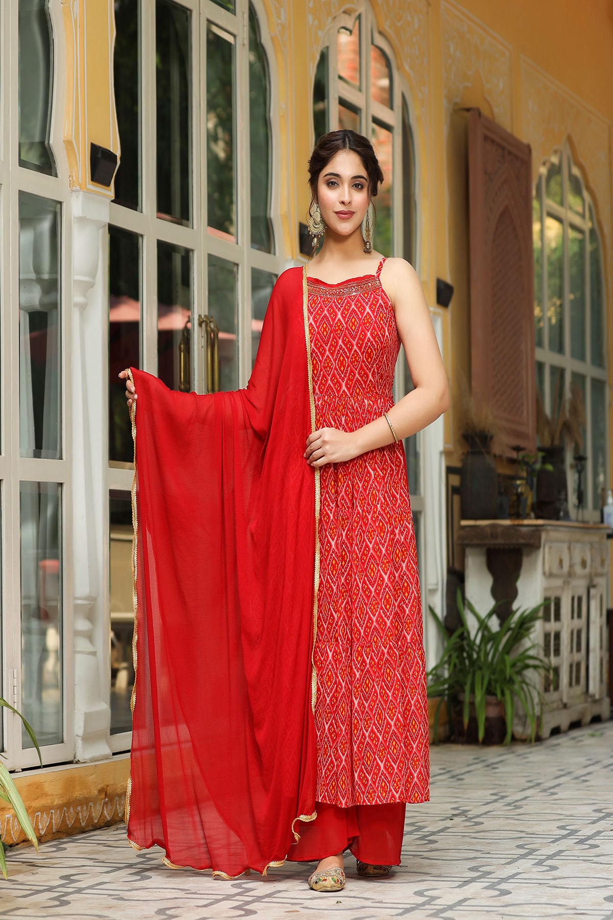 Woman in a red traditional outfit standing in front of a decorative building.