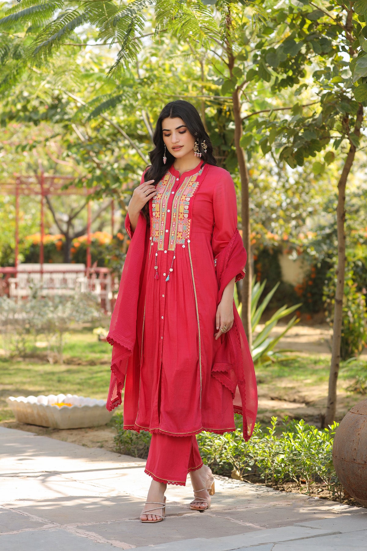 Woman in a red traditional outfit standing outdoors with greenery in the background