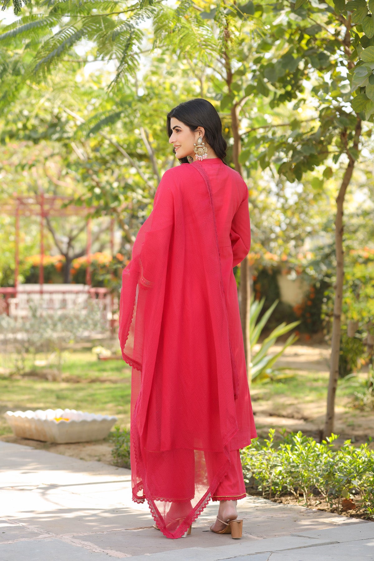 Woman in a red outfit standing in a garden with greenery around