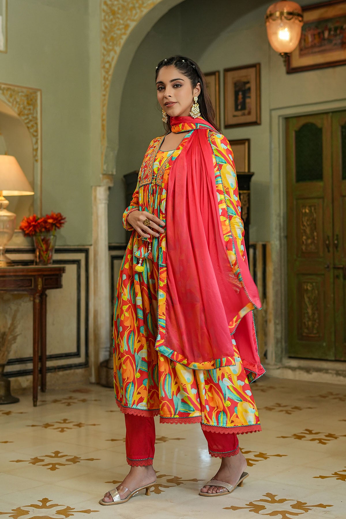 Woman in a colorful traditional outfit standing in an ornate room.