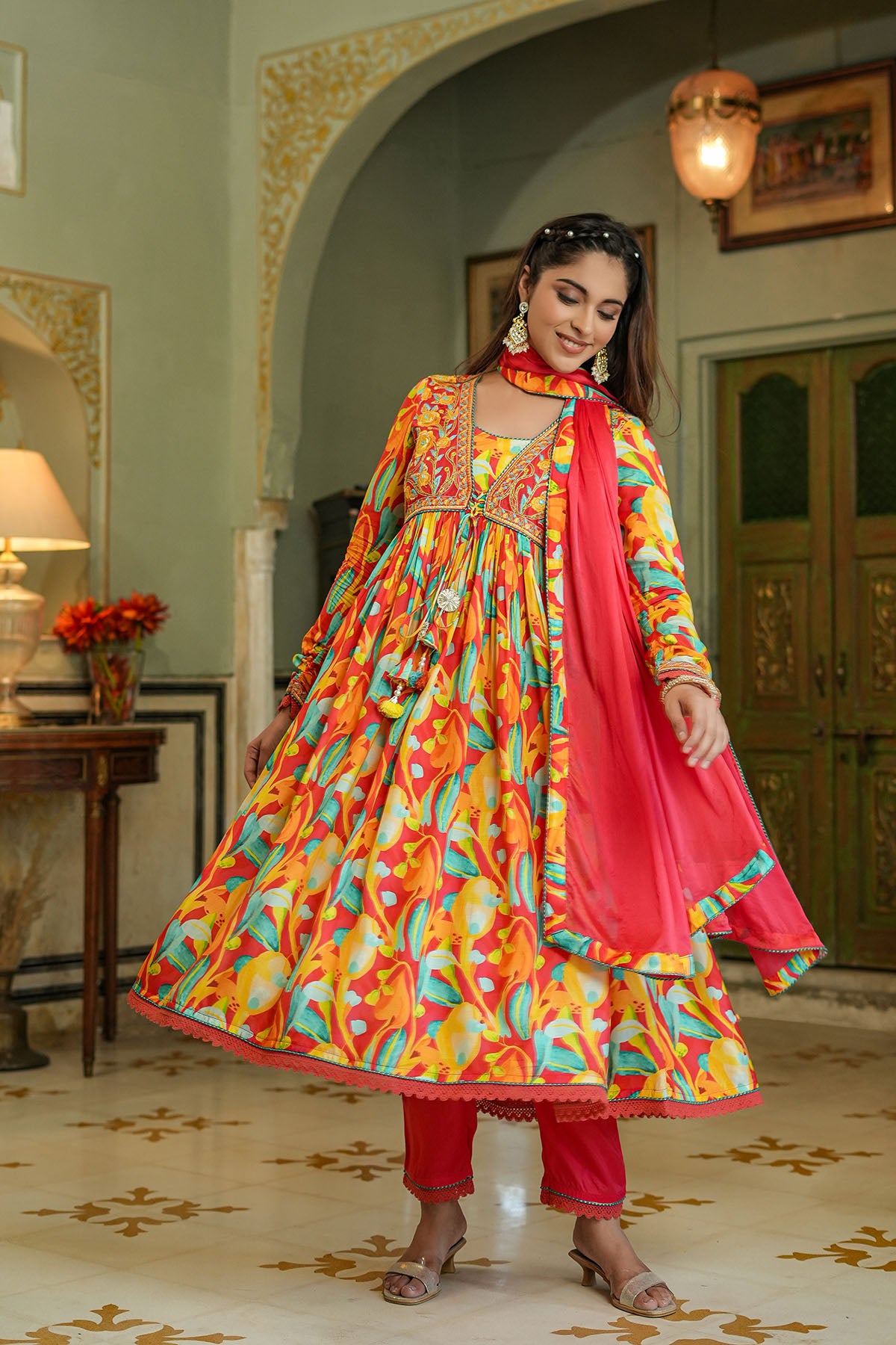 Woman in a colorful traditional outfit standing in an ornate room.
