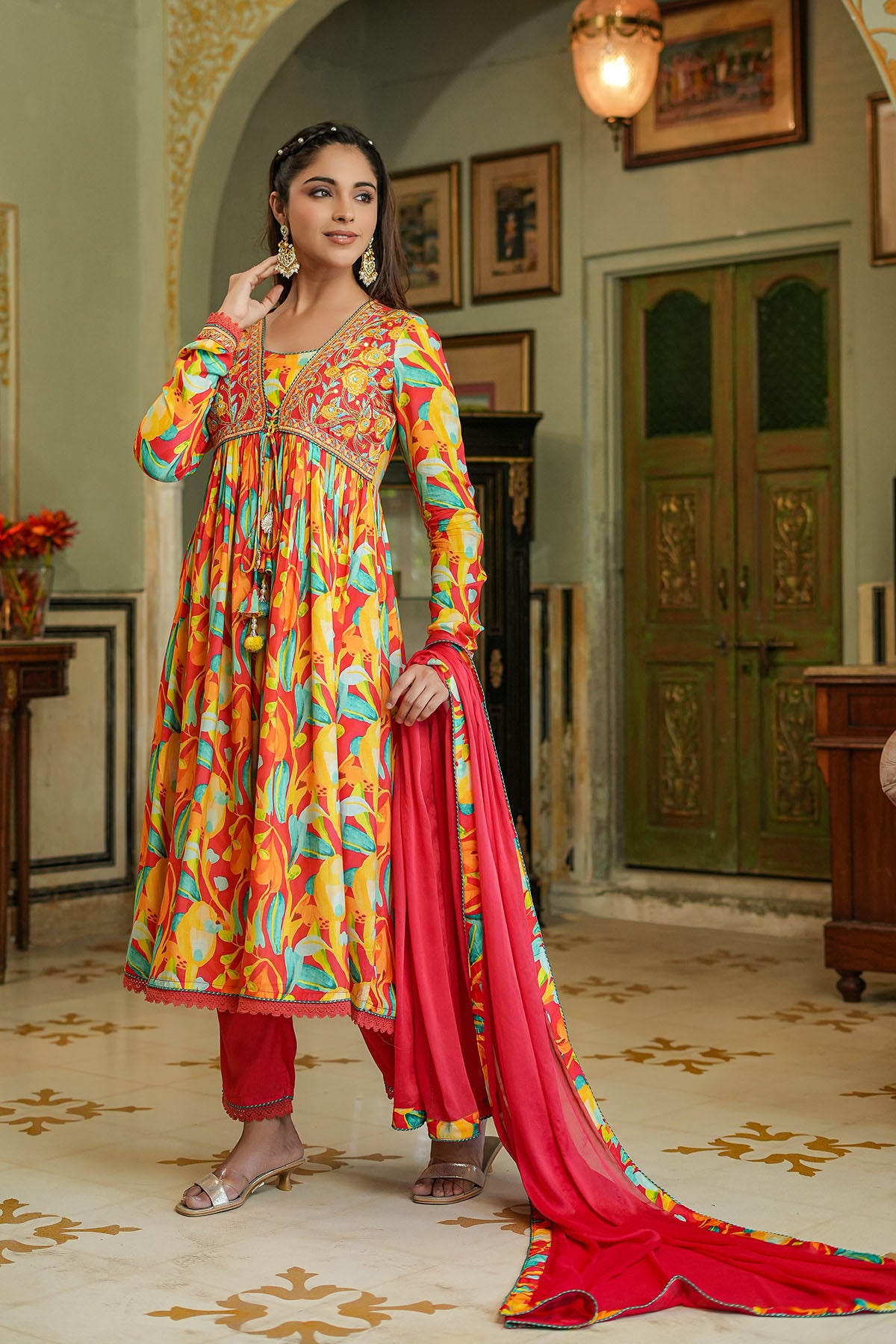 Woman in a colorful traditional outfit standing in an ornate room.