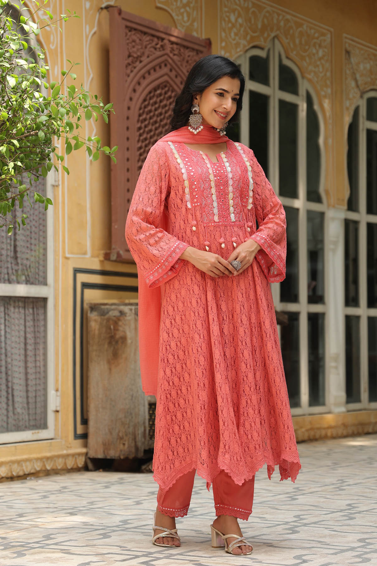 Woman in a coral pink traditional outfit standing in front of an ornate building.