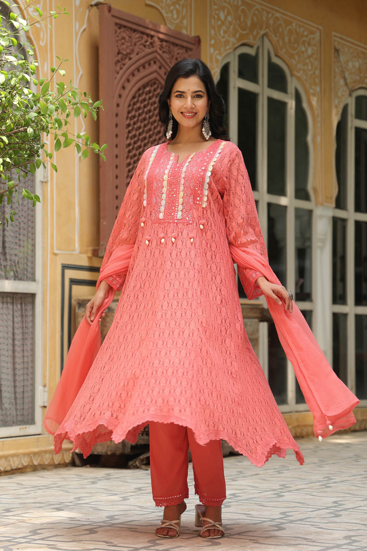 Woman wearing a pink traditional outfit with intricate designs in an outdoor setting.