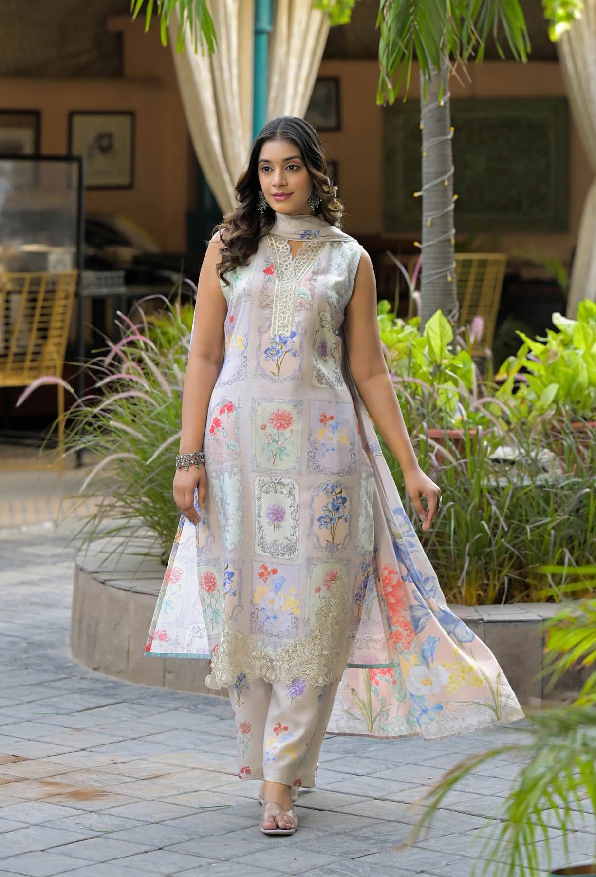 Woman in a floral dress standing outdoors with plants and a building in the background
