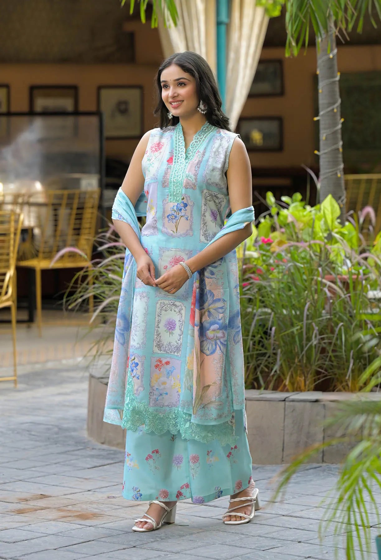 Woman in a light blue traditional outfit with floral patterns standing outdoors.