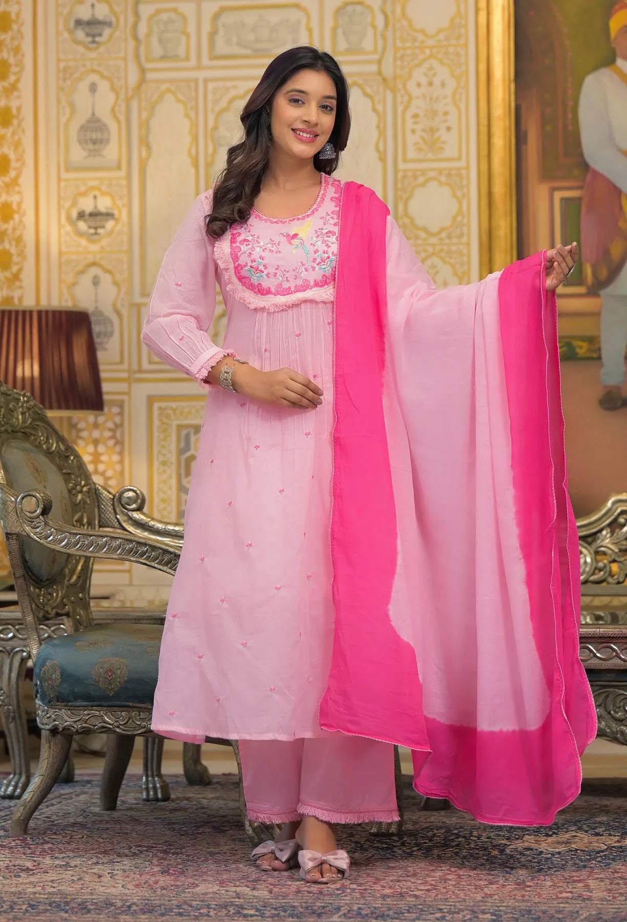 Woman in a pink traditional outfit with a matching dupatta in a decorated room.