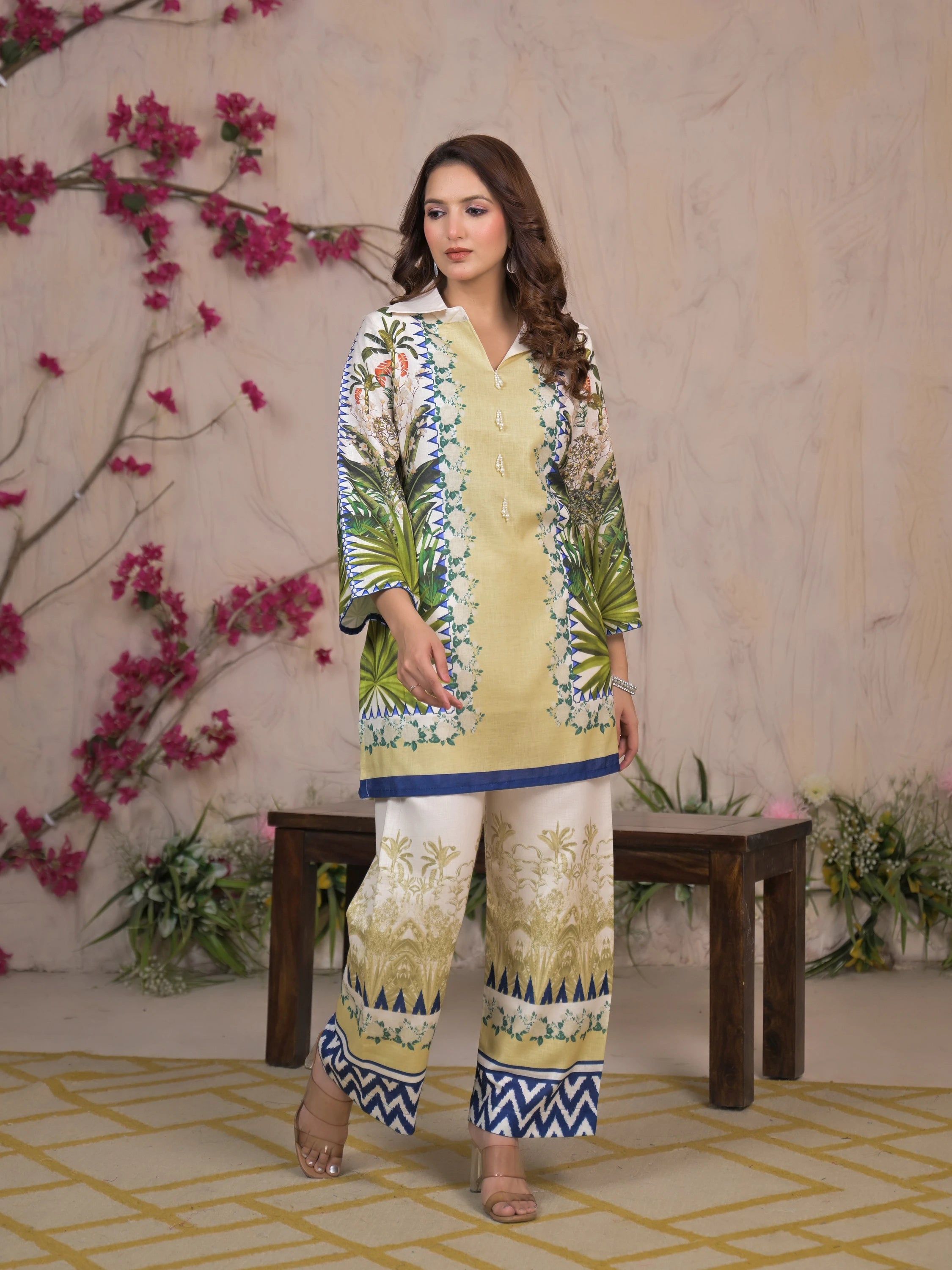 Woman in a floral outfit standing in front of a decorative background with flowers.