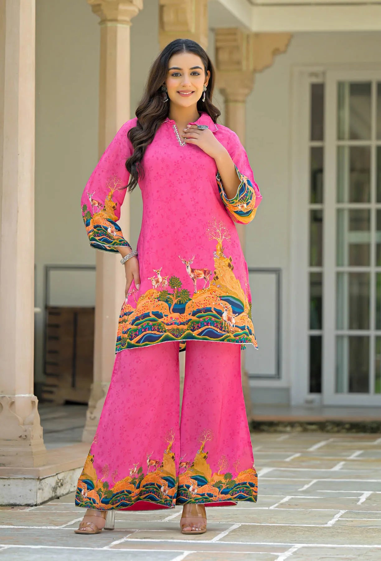Woman wearing a bright pink traditional outfit with colorful embroidery in an outdoor setting.