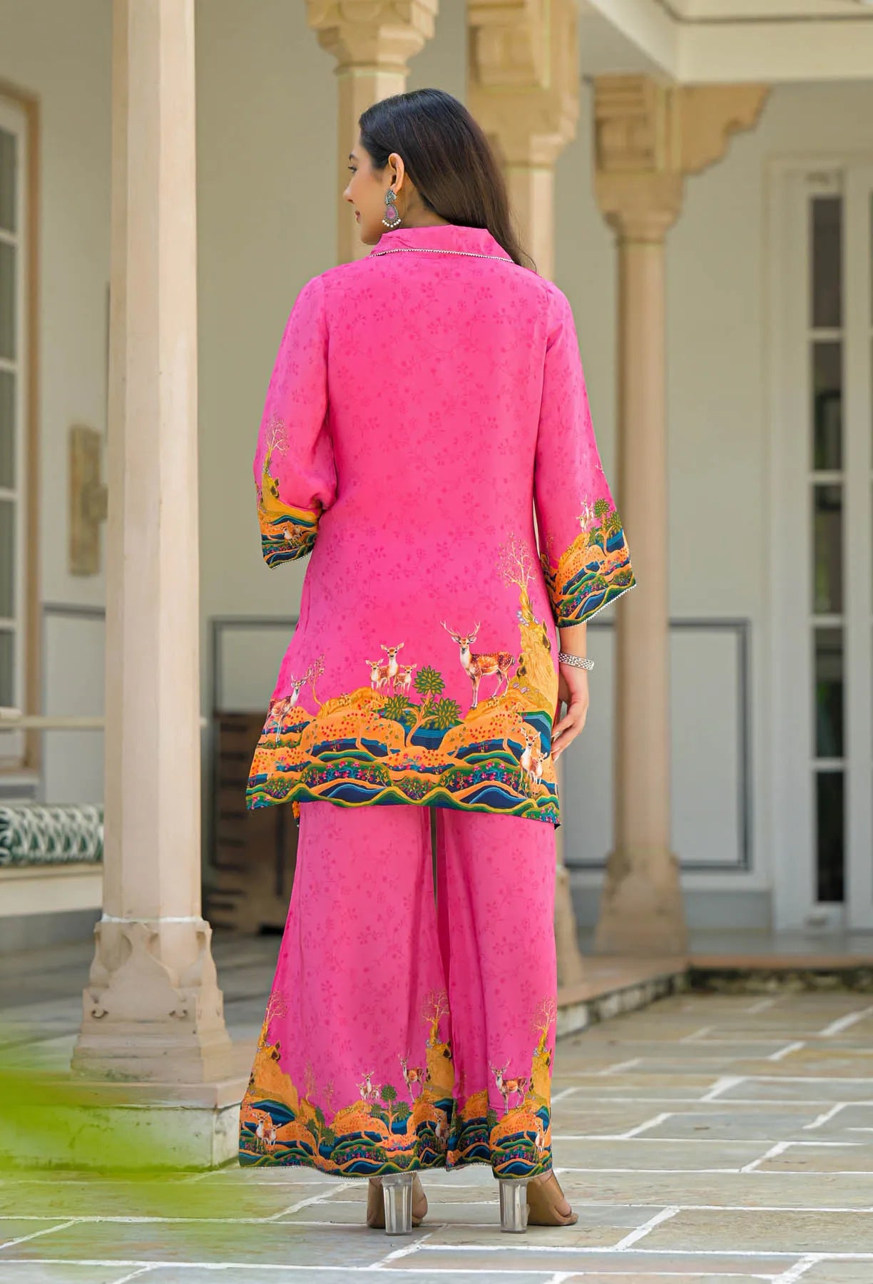 Woman wearing a bright pink traditional outfit with colorful patterns in an outdoor setting. back side