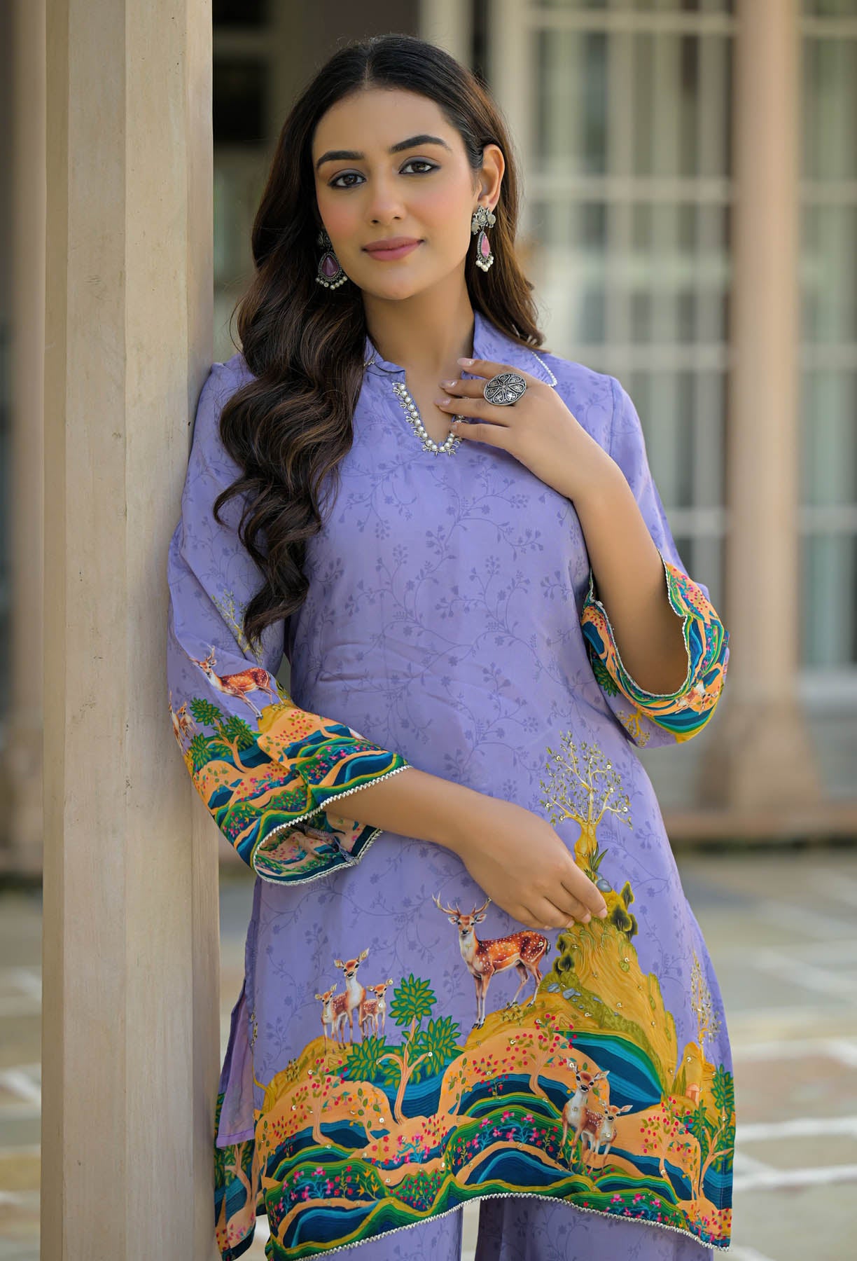Woman wearing a purple embroidered outfit with a scenic design, standing indoors.