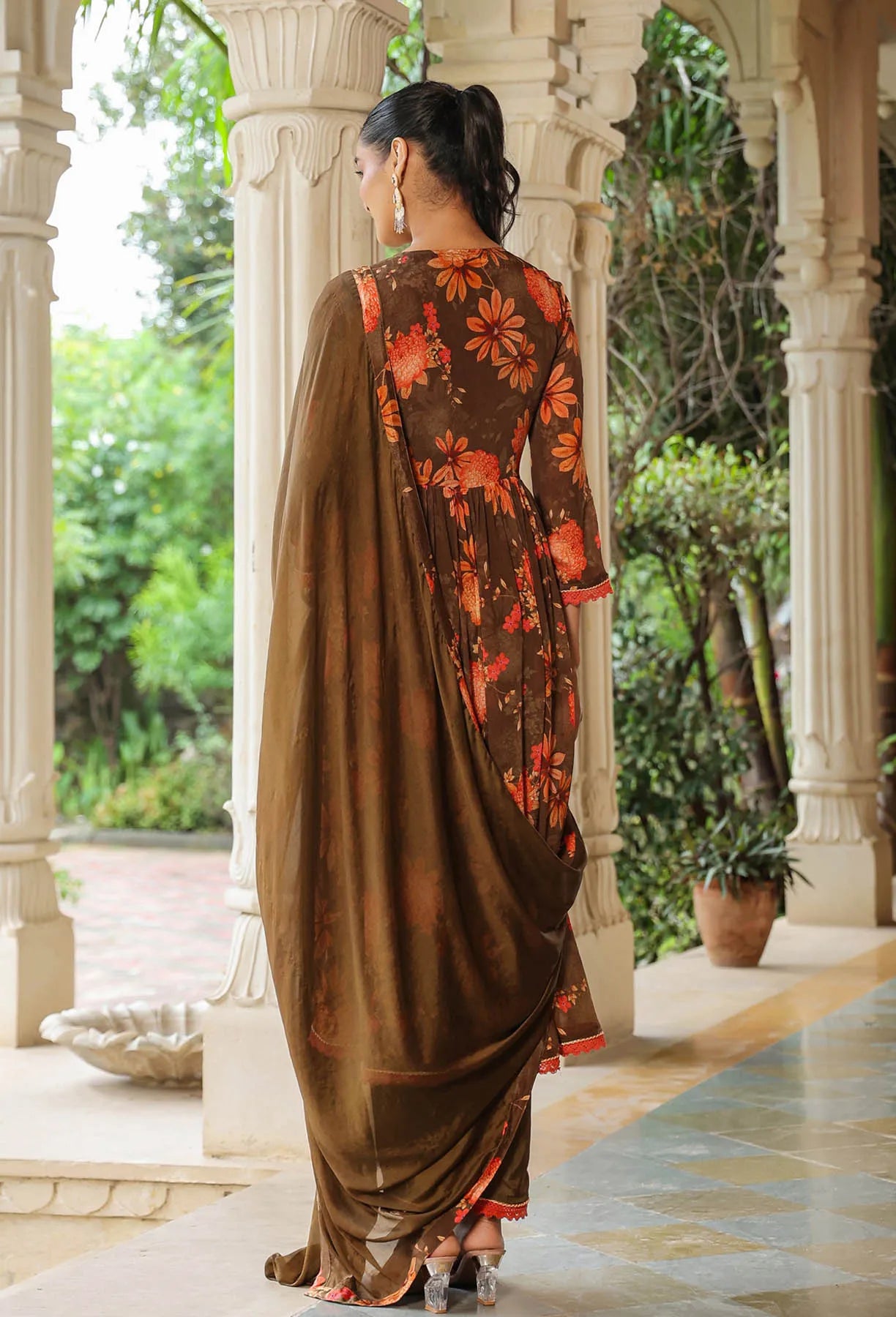 Woman in a brown saree with floral patterns standing in an outdoor setting.