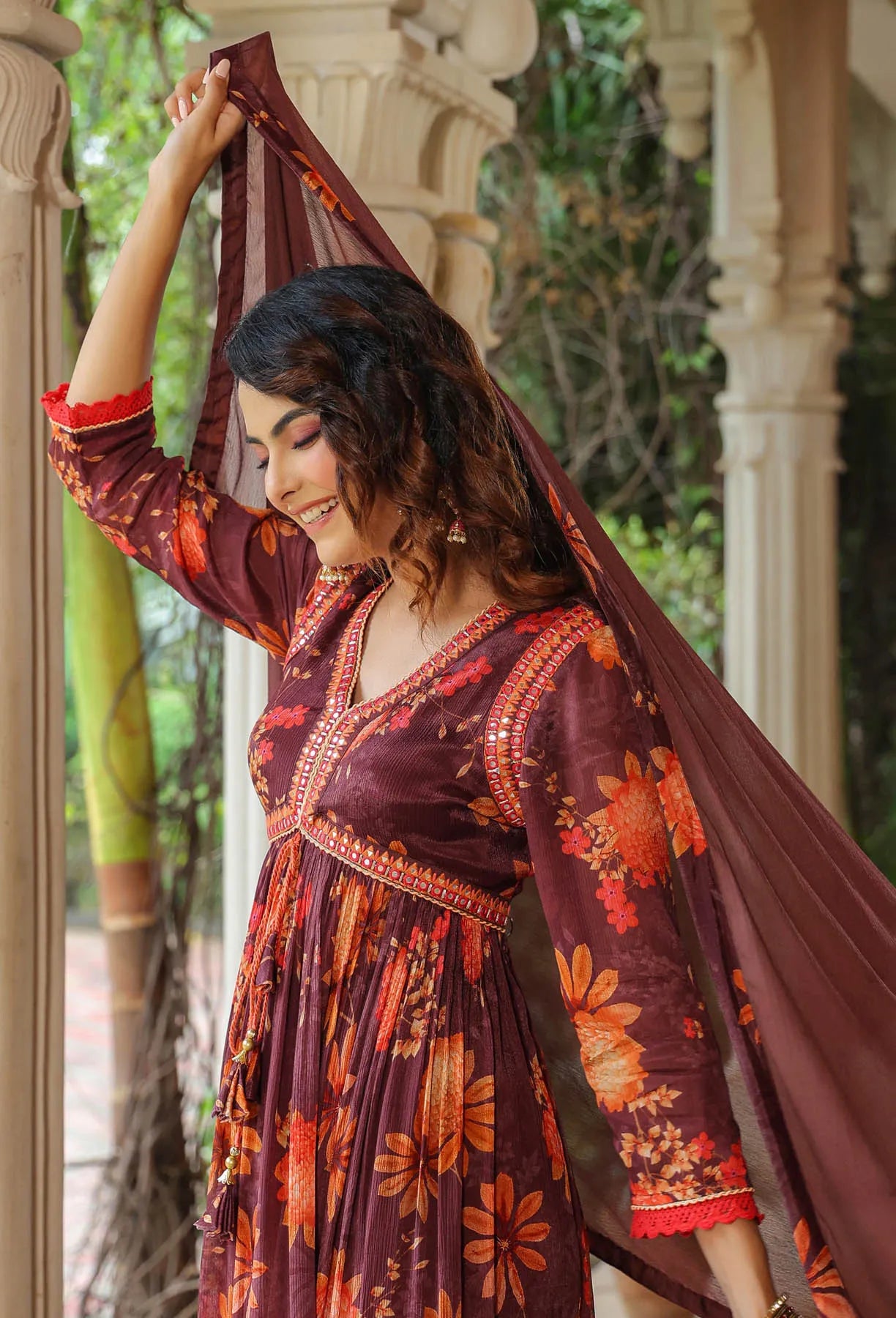 Woman in a floral dress with a long scarf, standing outdoors.