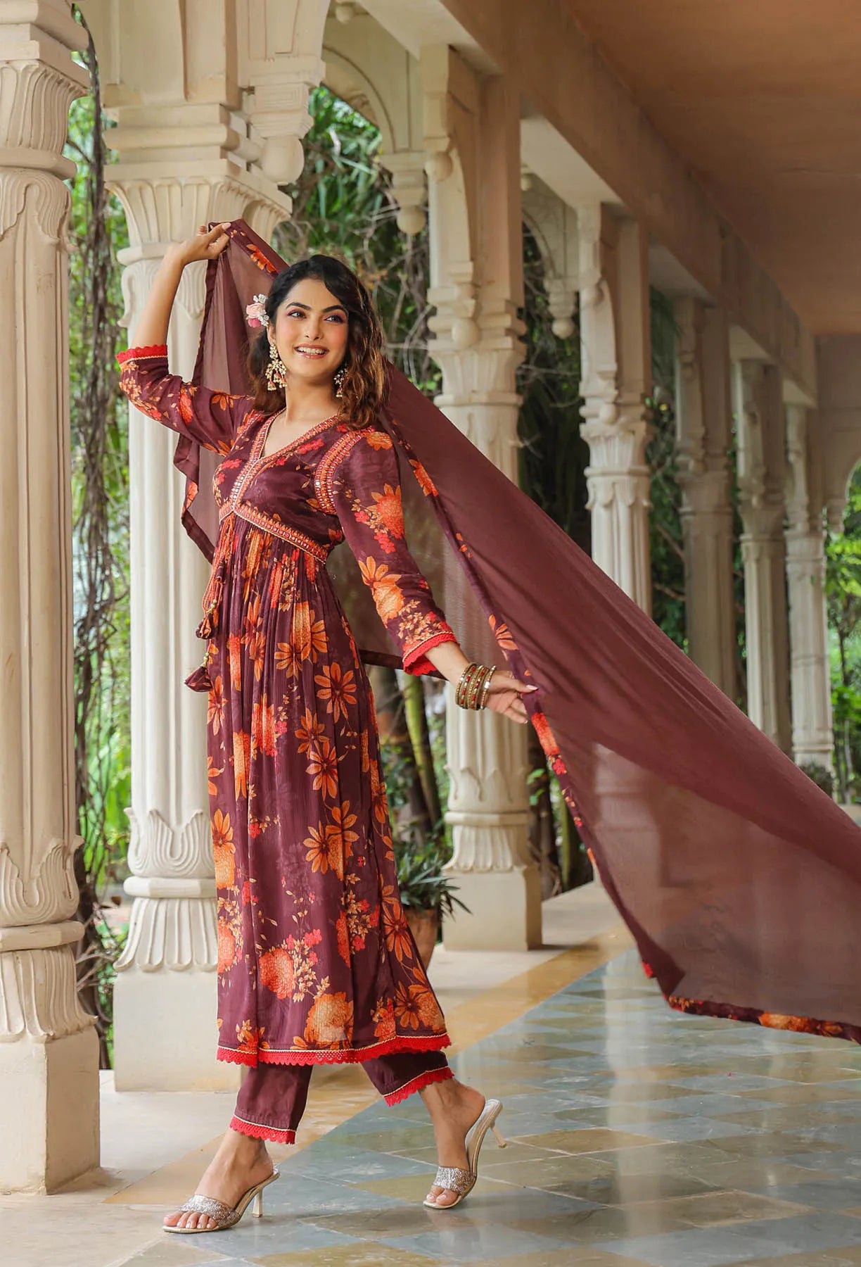 Woman in a traditional outfit with a long scarf standing in an elegant outdoor setting.