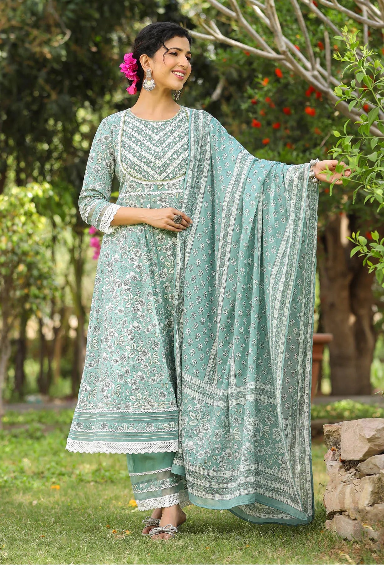 Woman in a light blue traditional outfit with white patterns standing outdoors.