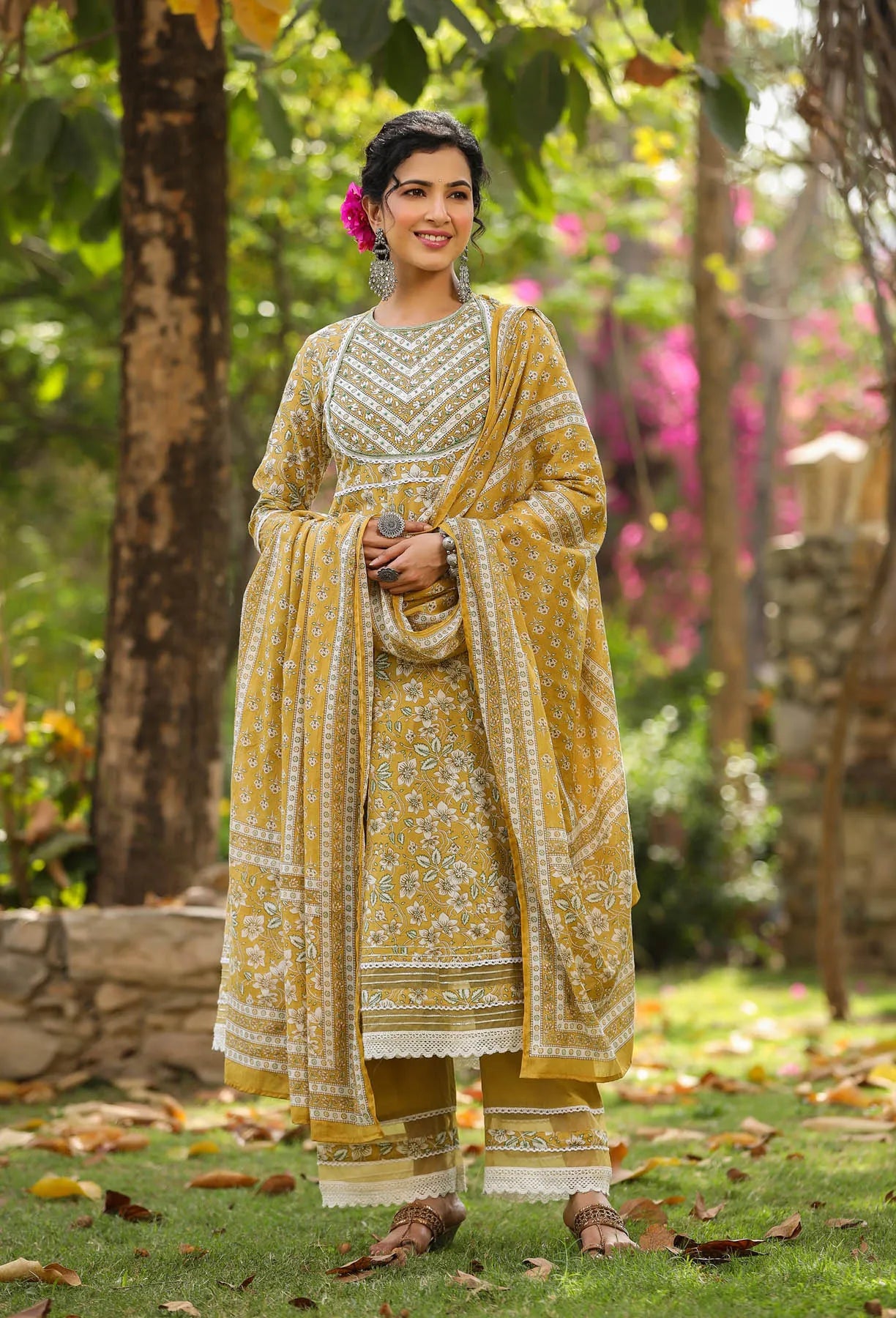 Woman in a yellow and white traditional outfit standing in a garden.