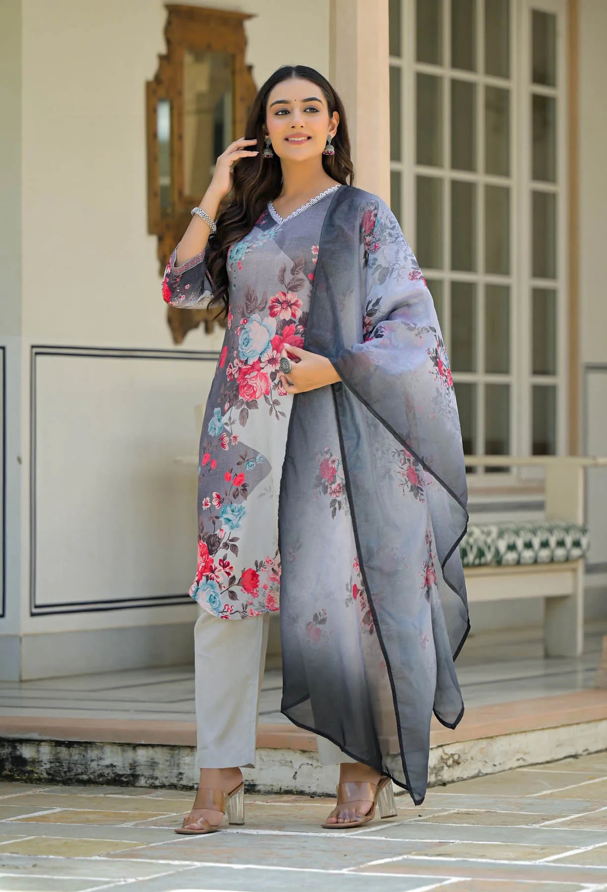 Woman wearing a floral outfit with a gray dupatta in front of a building.