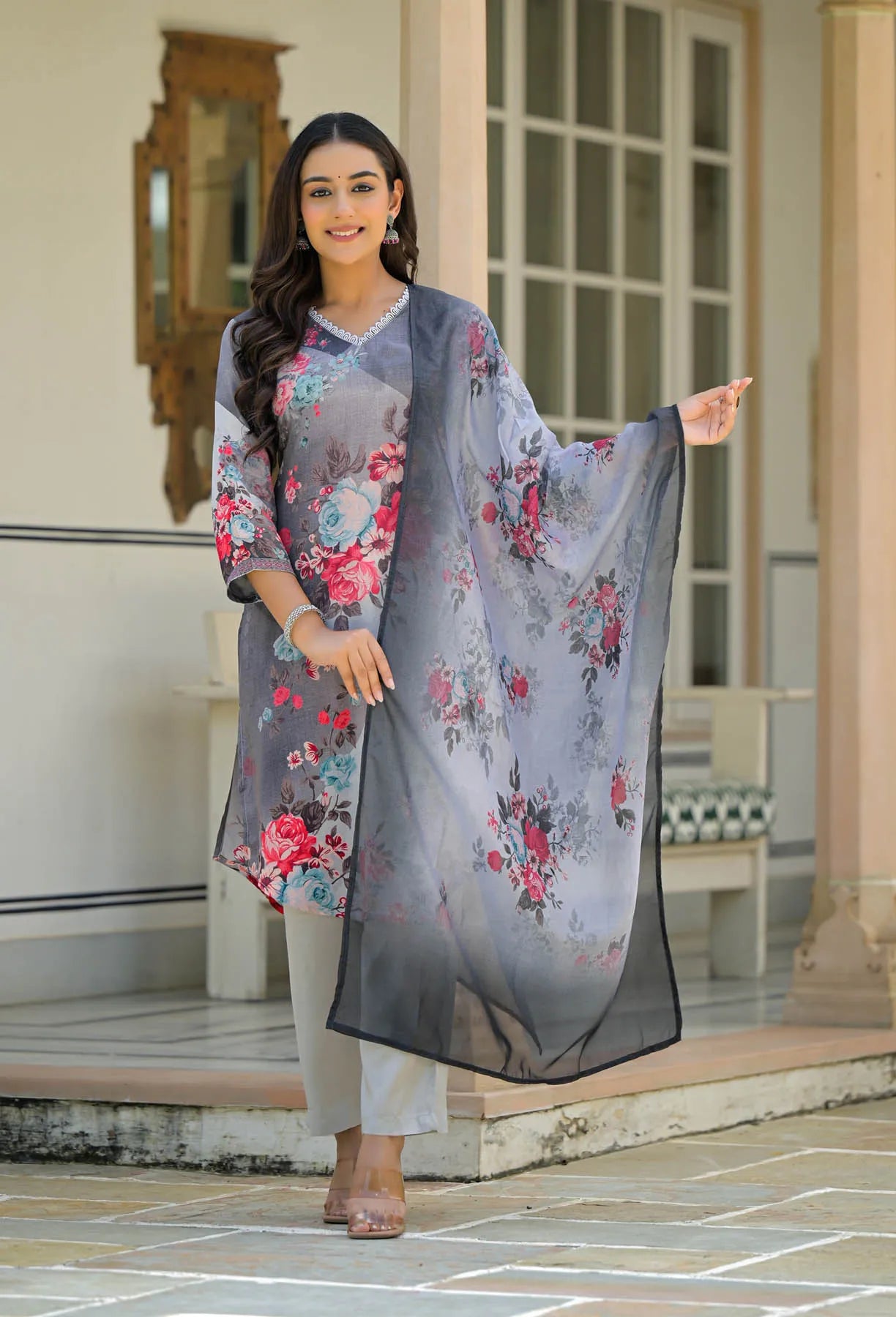 Woman holding a floral dupatta in front of a building entrance