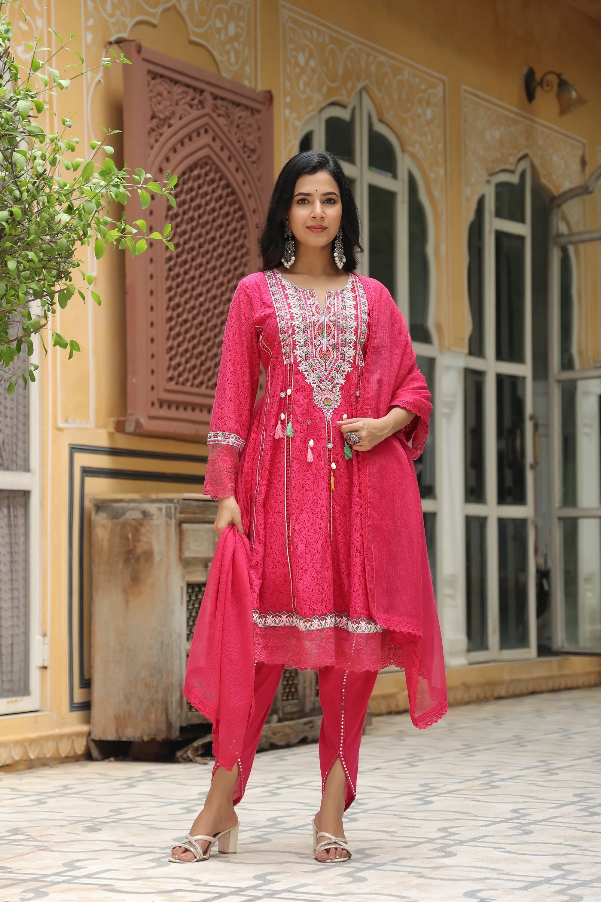 Woman in a pink traditional outfit standing in front of an ornate building.