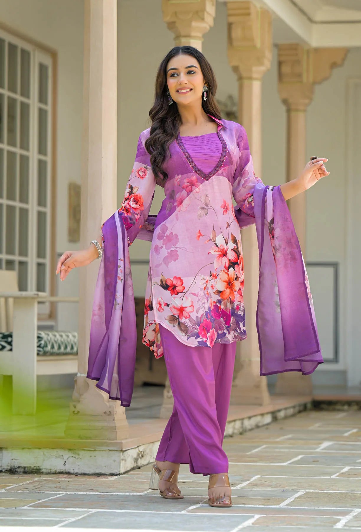 Woman in a floral dress with a purple dupatta standing in an outdoor setting.