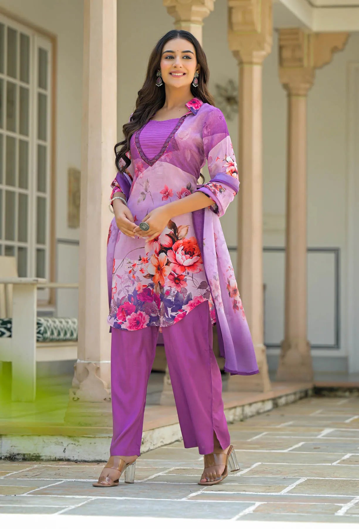 Woman in a purple floral outfit standing in front of a traditional building.