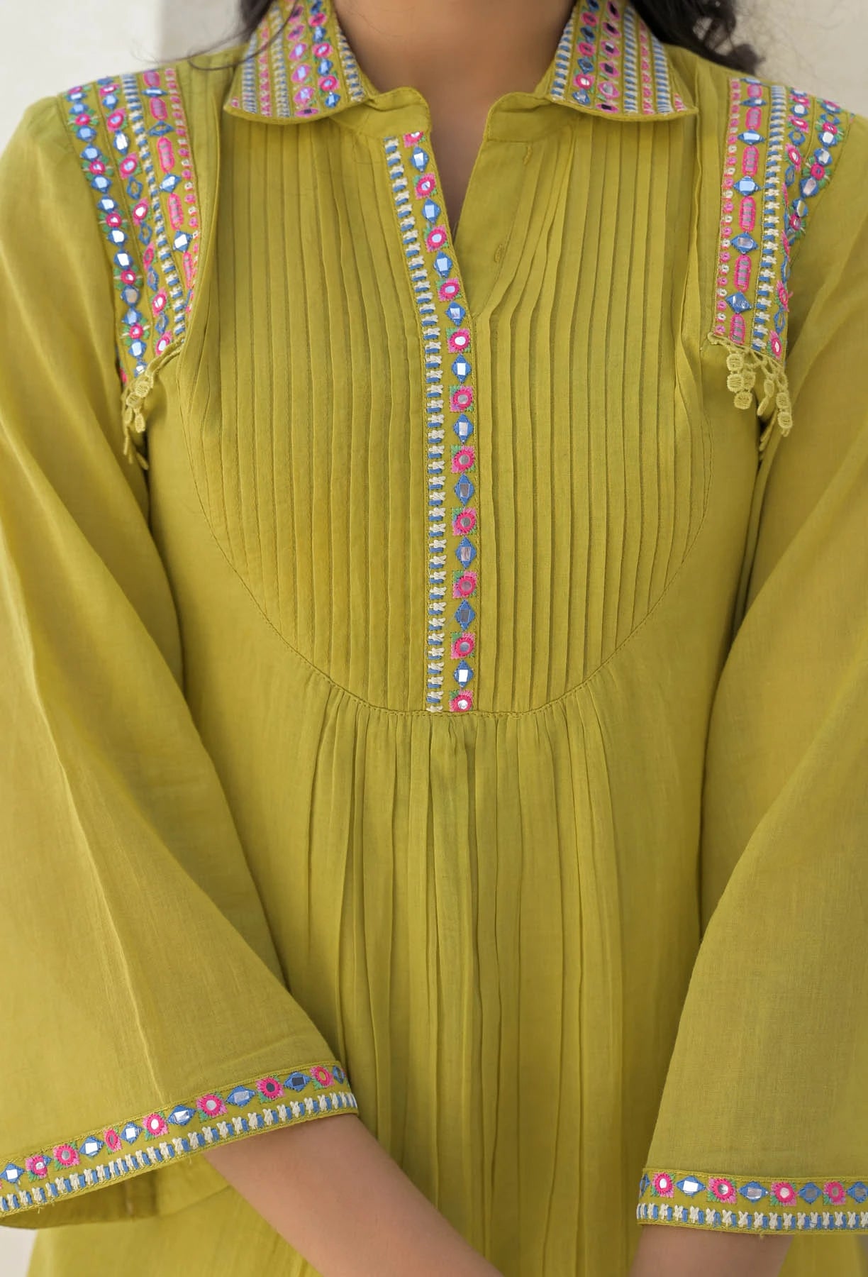 Green traditional outfit with colorful embroidery on a plain background