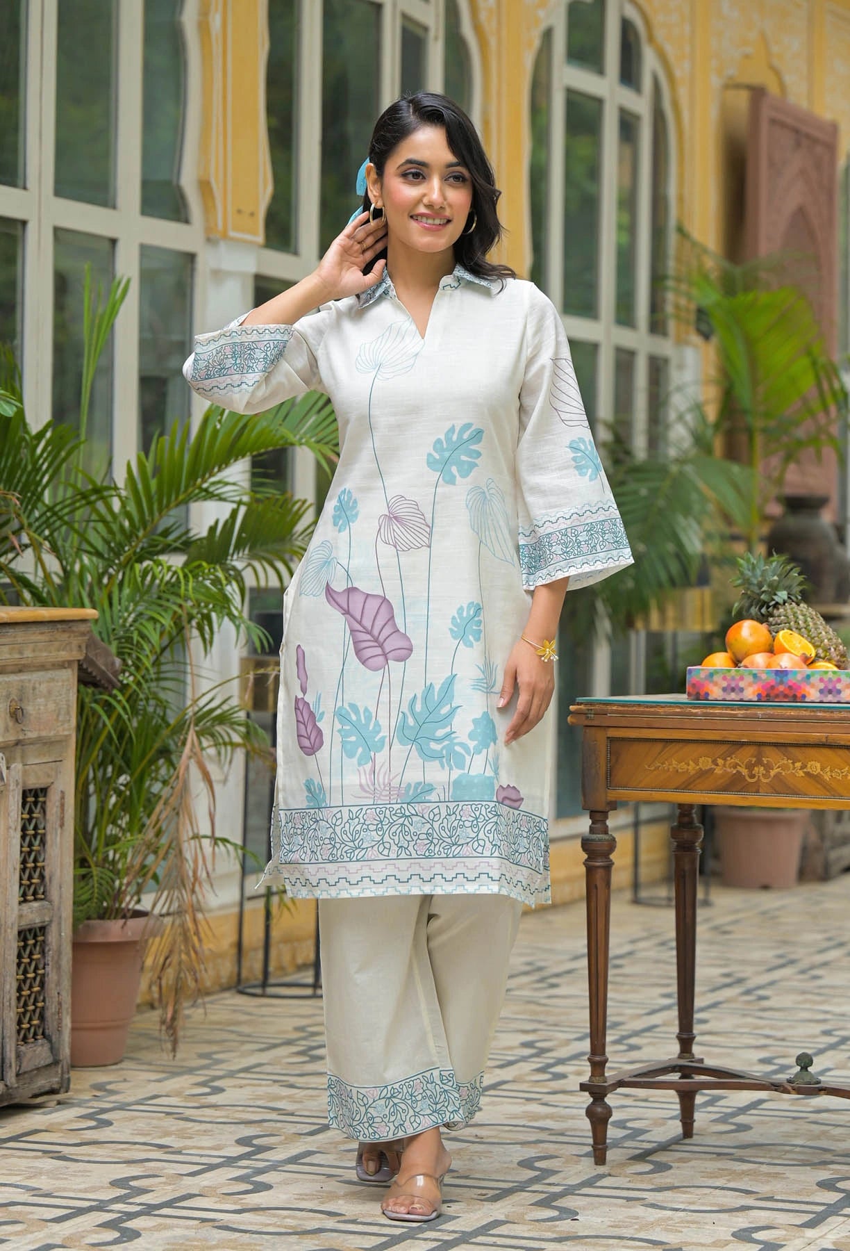 Woman in a white floral kurta with beige pants standing in an outdoor setting.