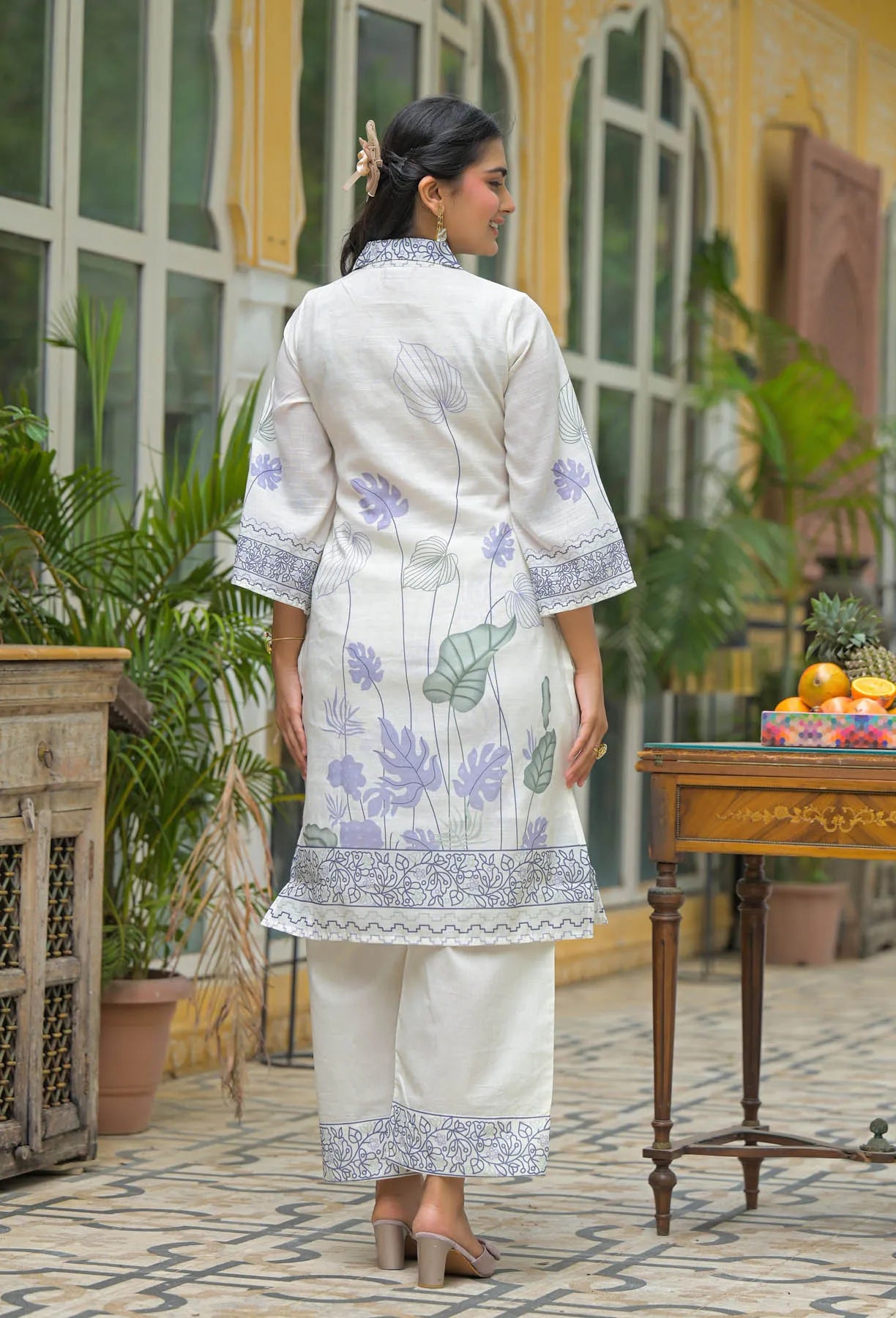 Woman in a white traditional outfit with floral patterns standing in an outdoor setting.