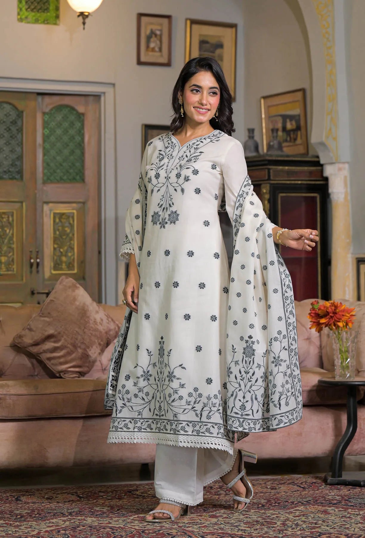 Woman in a white embroidered traditional outfit standing in a decorated room.